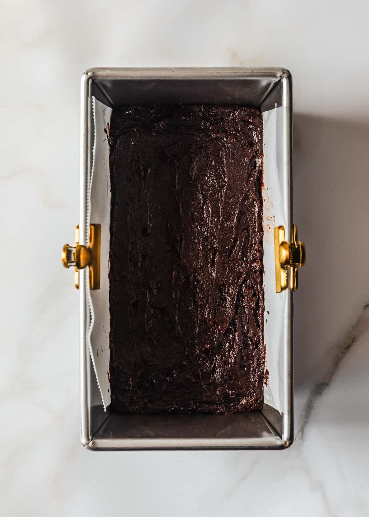 A loaf pan with small batch brownies batter on a white counter.
