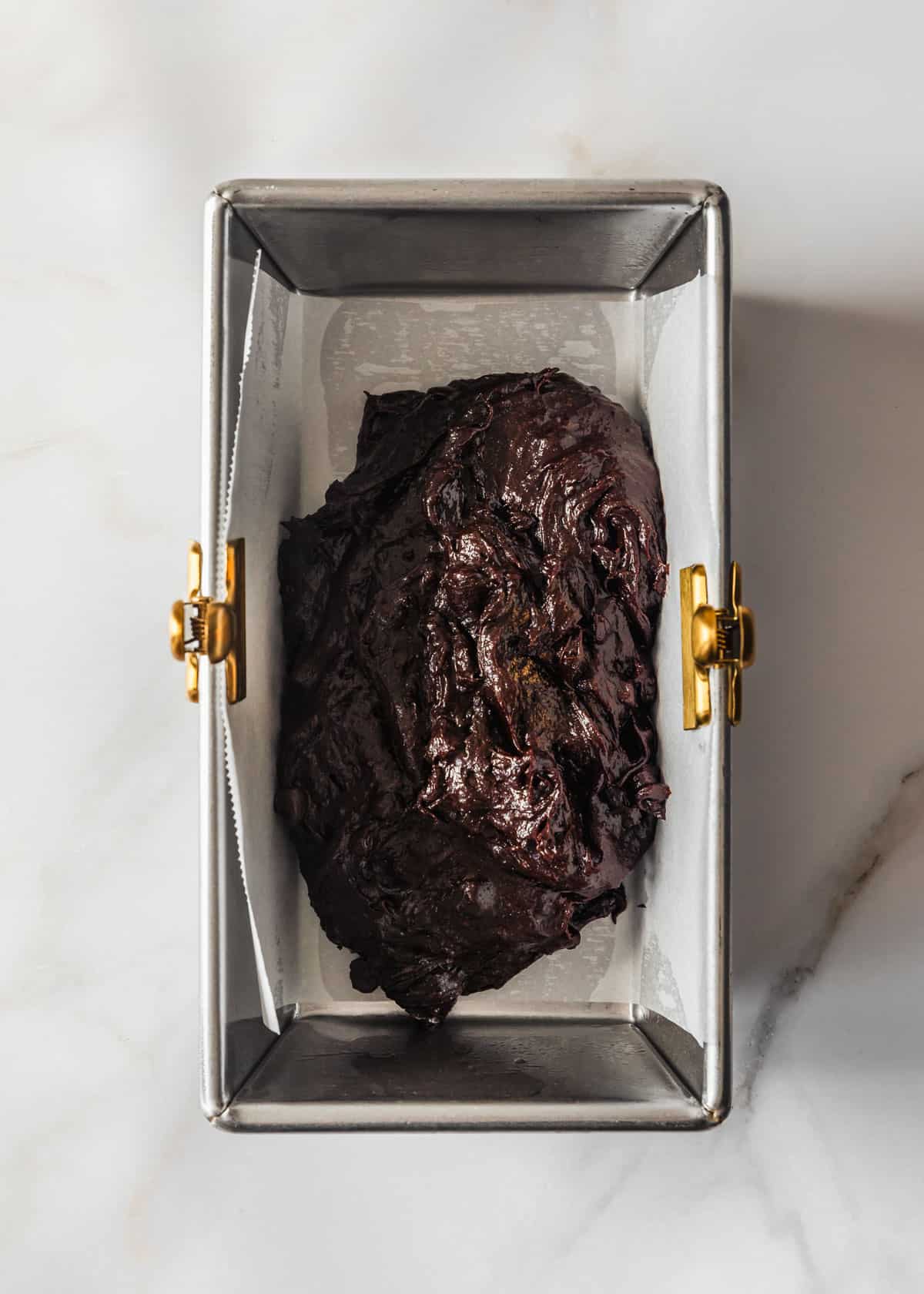 A loaf pan with brownie batter on a white counter.