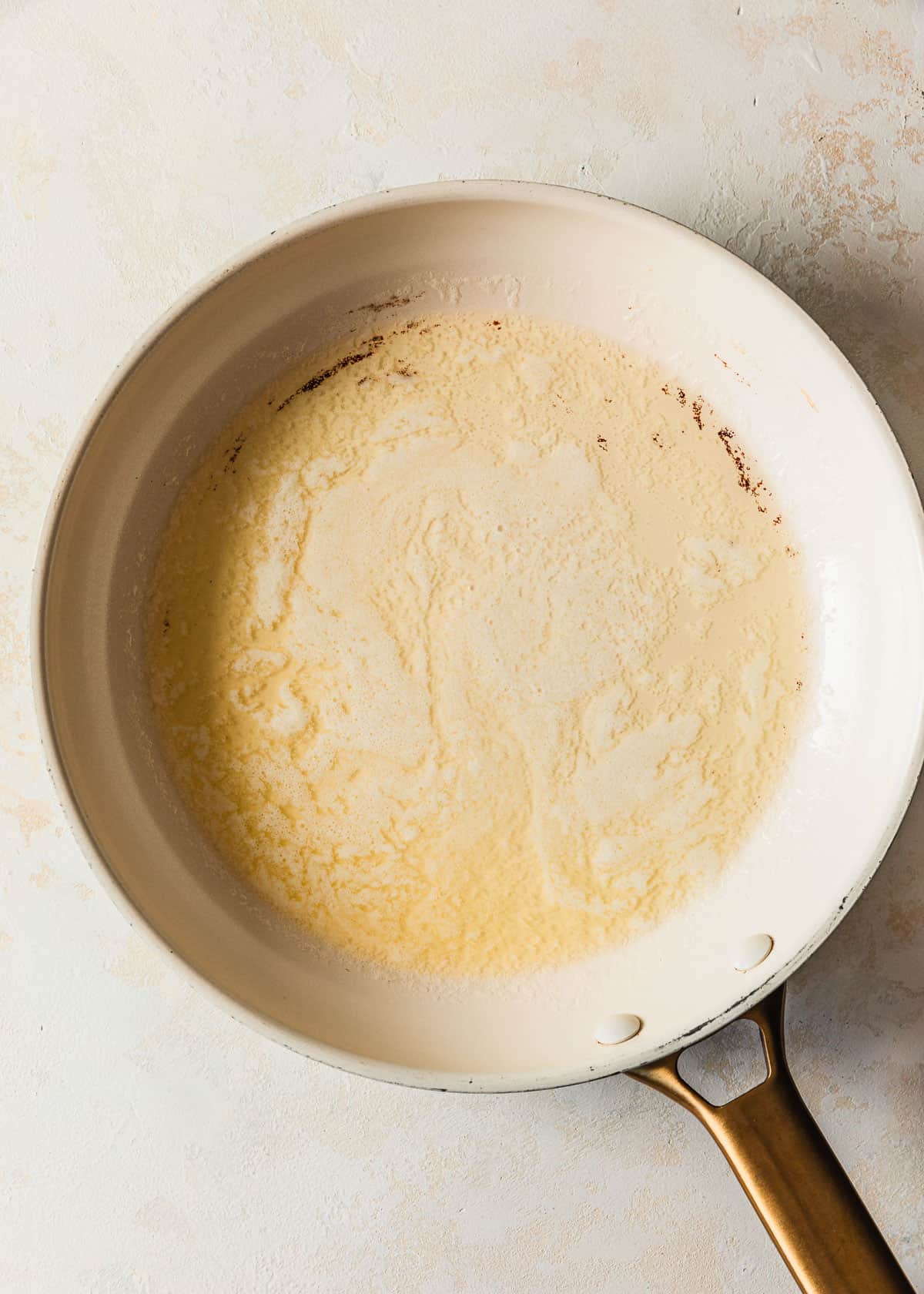 A white saucepan with melted butter on a tan counter.
