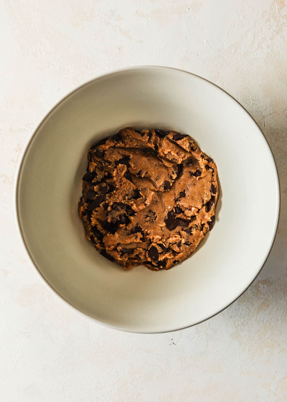 A white bowl of small-batch chocolate chip cookies dough on a tan counter.