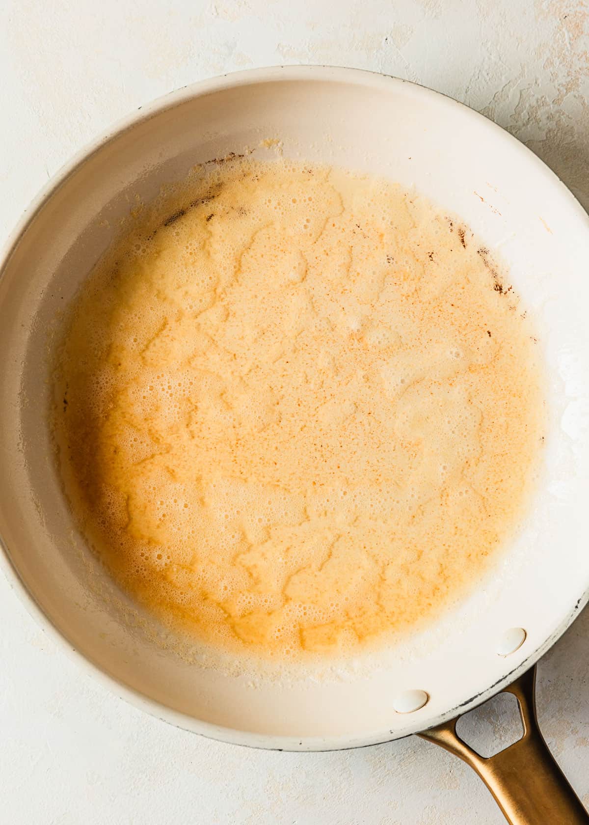 A white pan of brown butter on a beige backround.