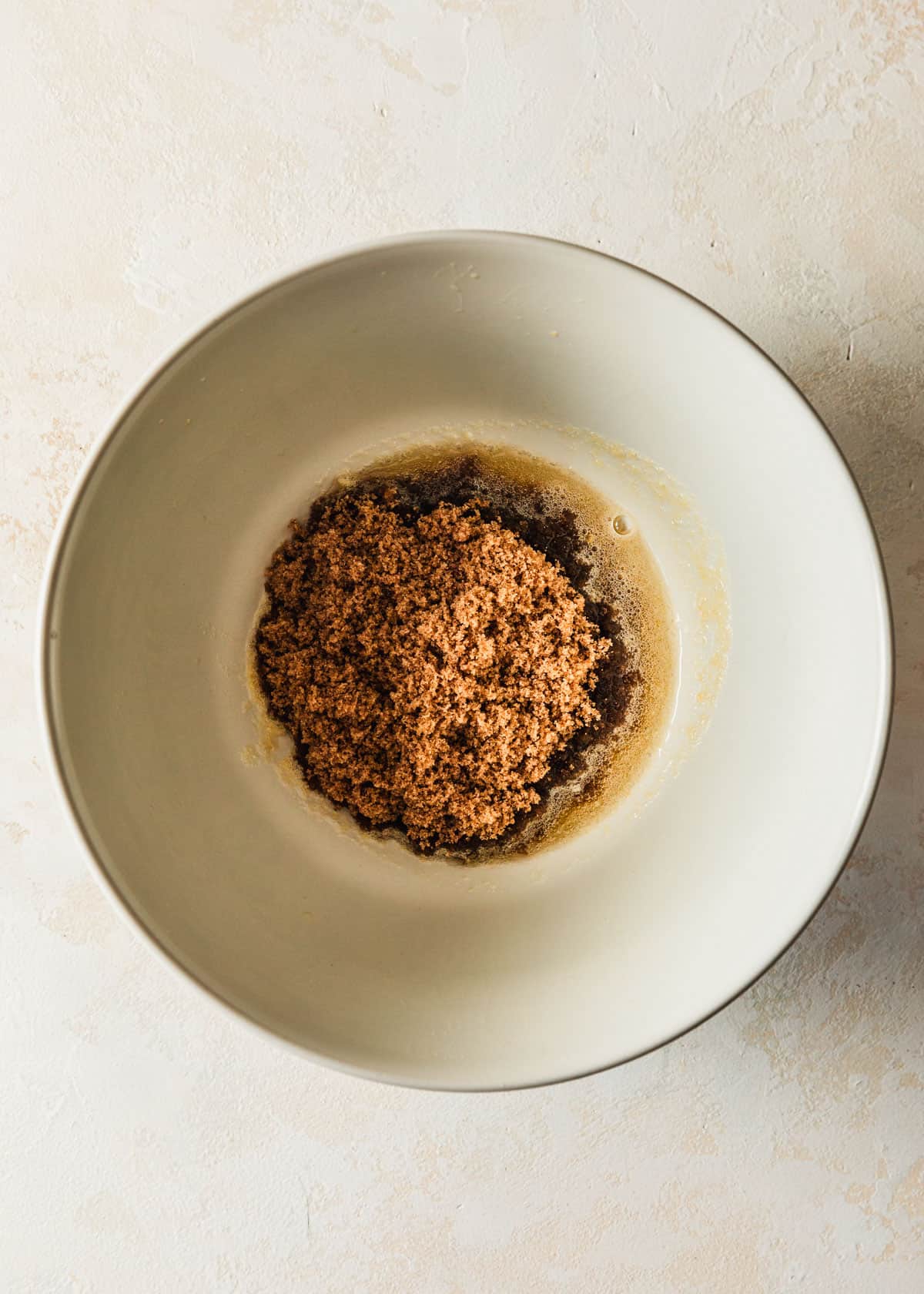 A white bowl with brown butter and sugar on a tan counter.