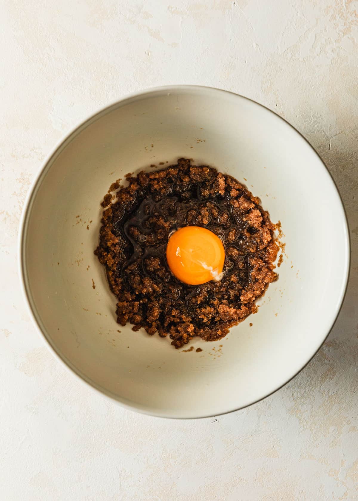 A white bowl with butter, sugar, and an egg yolk on a beige background.