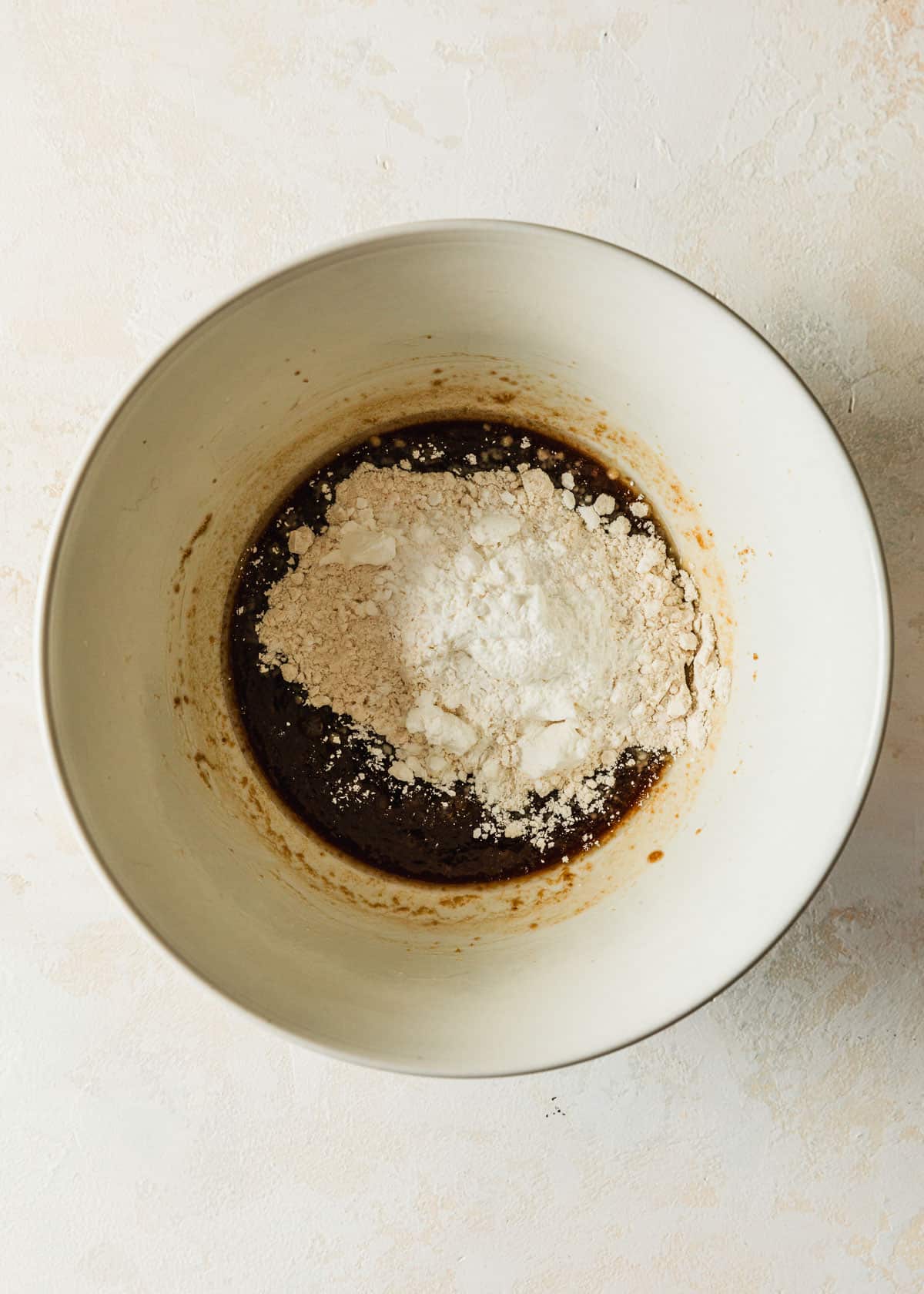 A white bowl of butter, sugar, and flour on a tan counter.