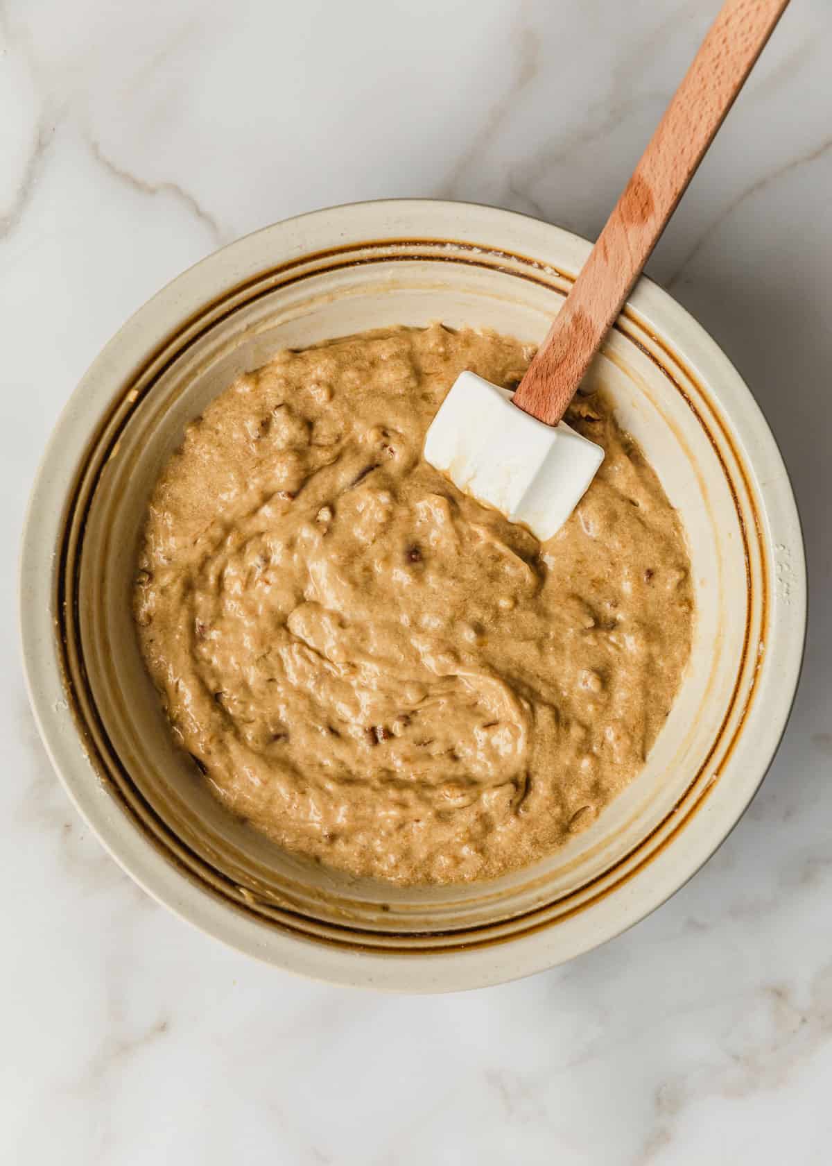 A white bowl of small batch banana muffins batter on a marble counter.