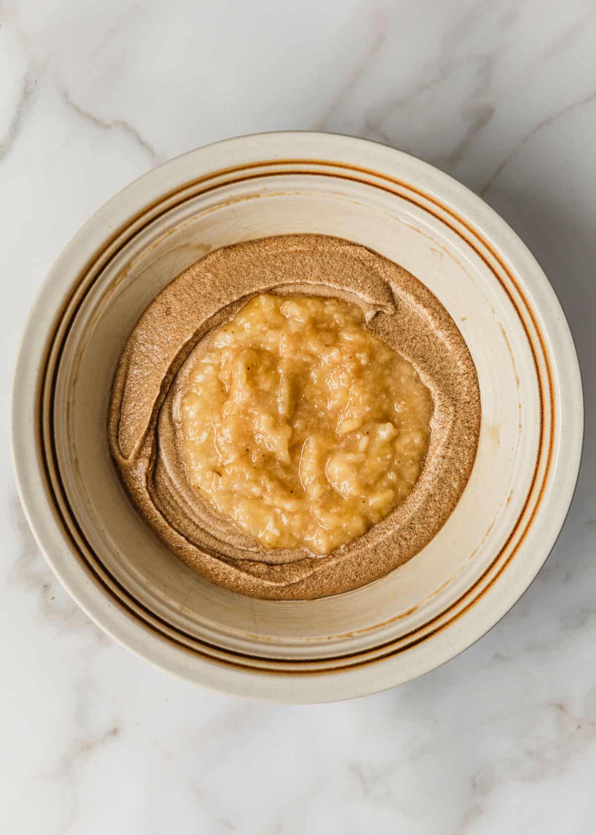 A white bowl of mixed butter, sugar, eggs, and bananas on a white counter.