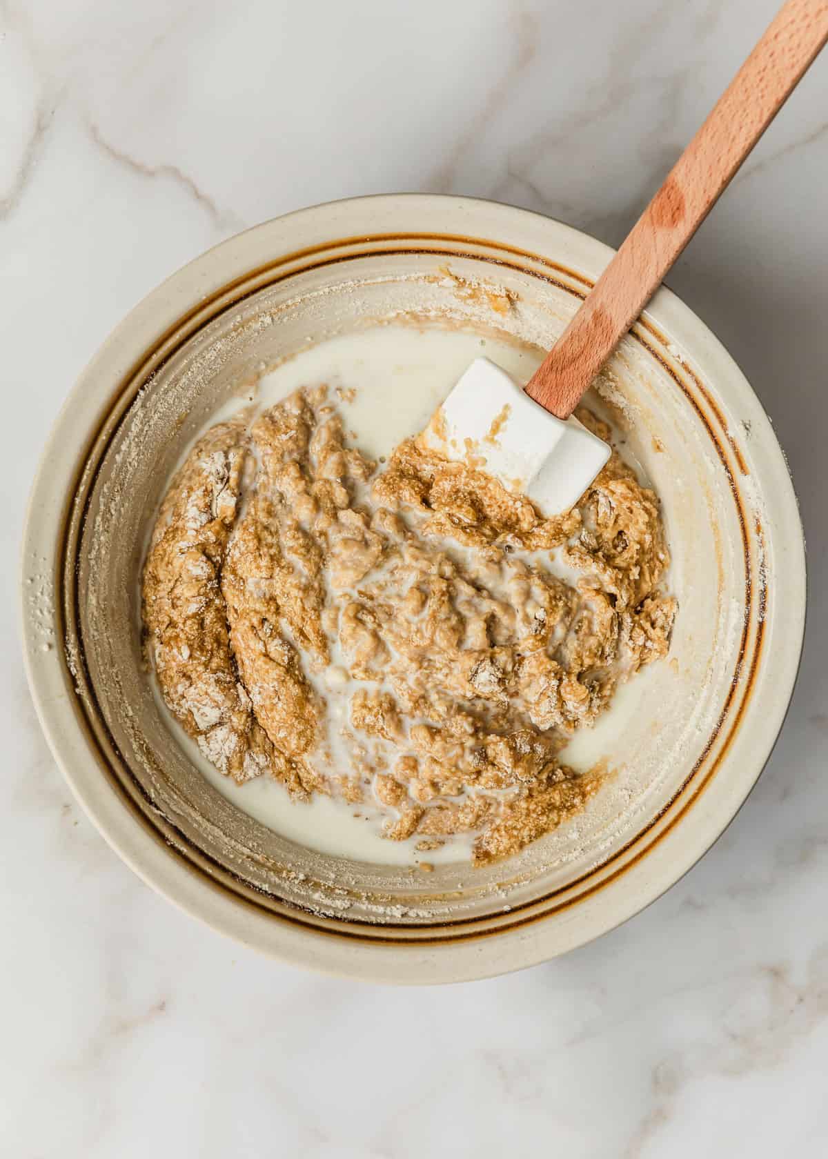 A white bowl of batter and milk on a marble table.