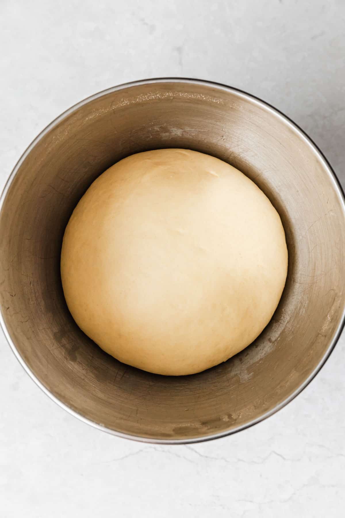 A silver bowl of puffy dough on a marble counter.