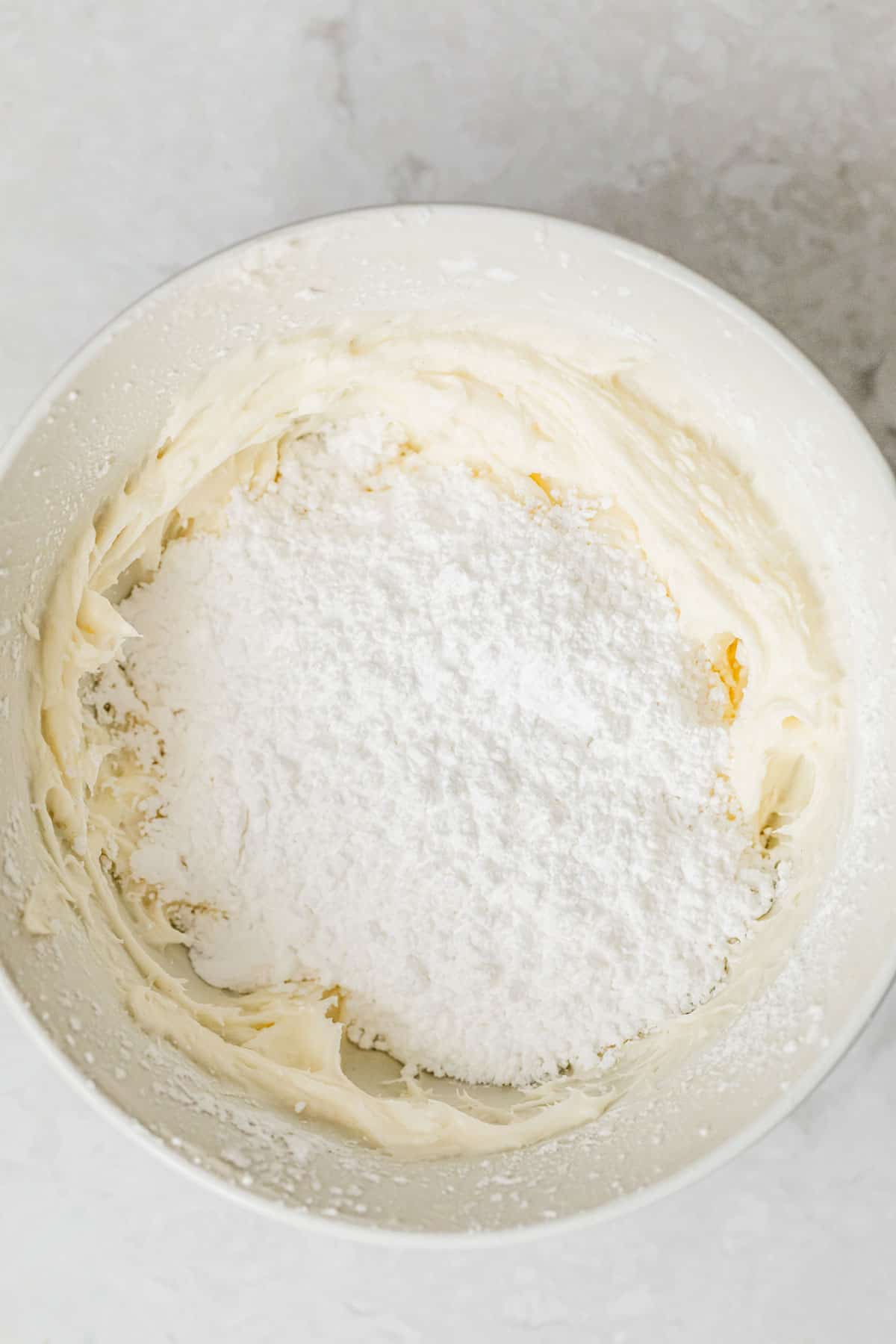 A white bowl of cream cheese and powdered sugar on a white counter.