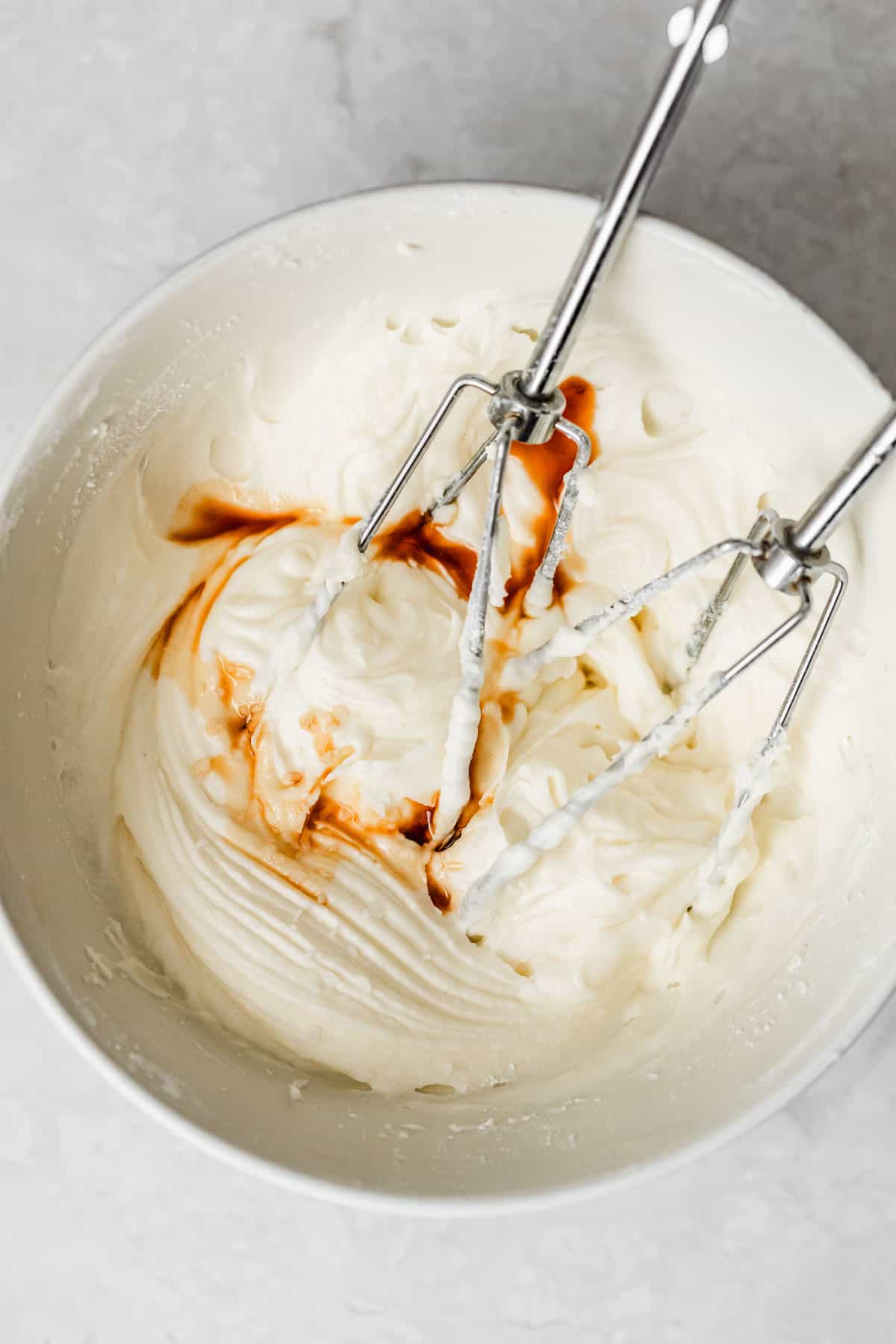 A white bowl of cream cheese frosting with vanilla on a marble table.