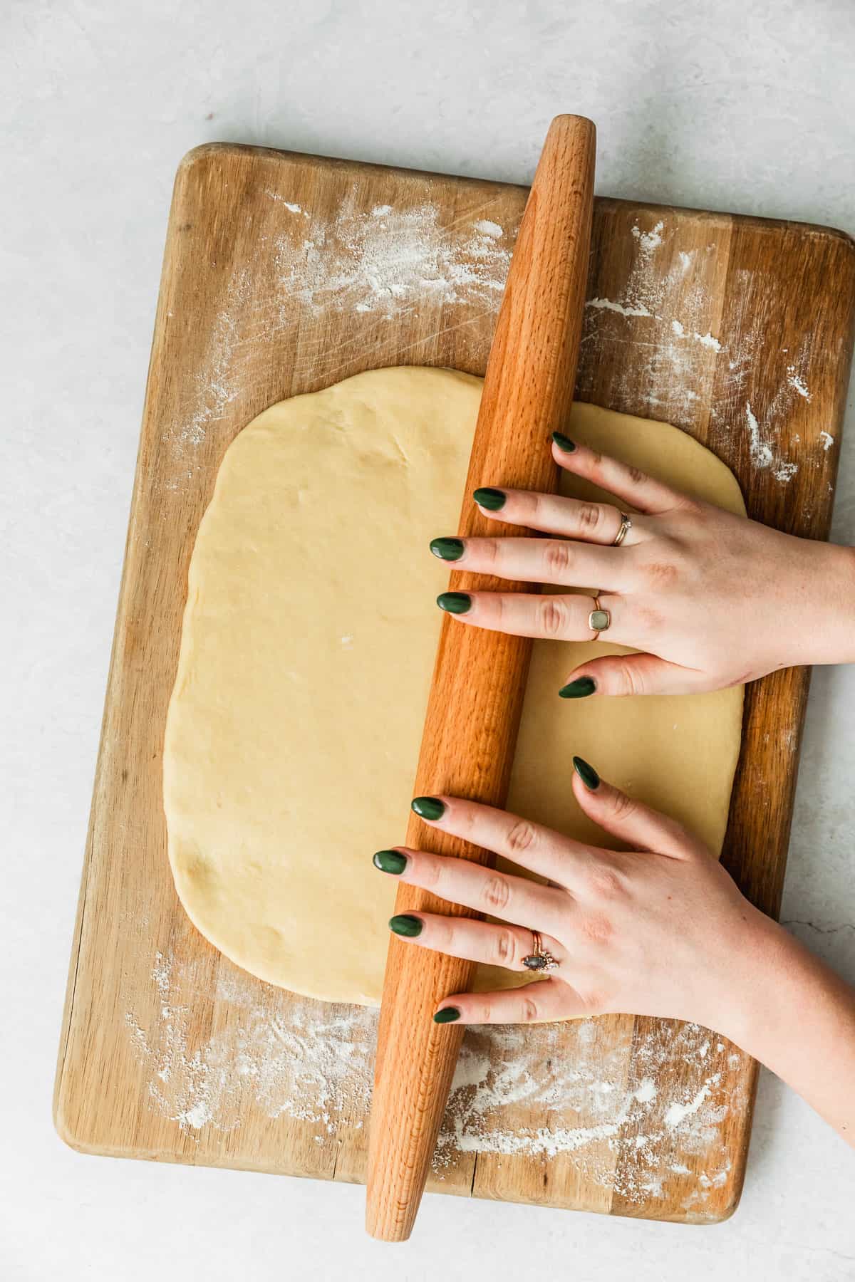 Hands using a rolling pin to roll dough on a wood board.