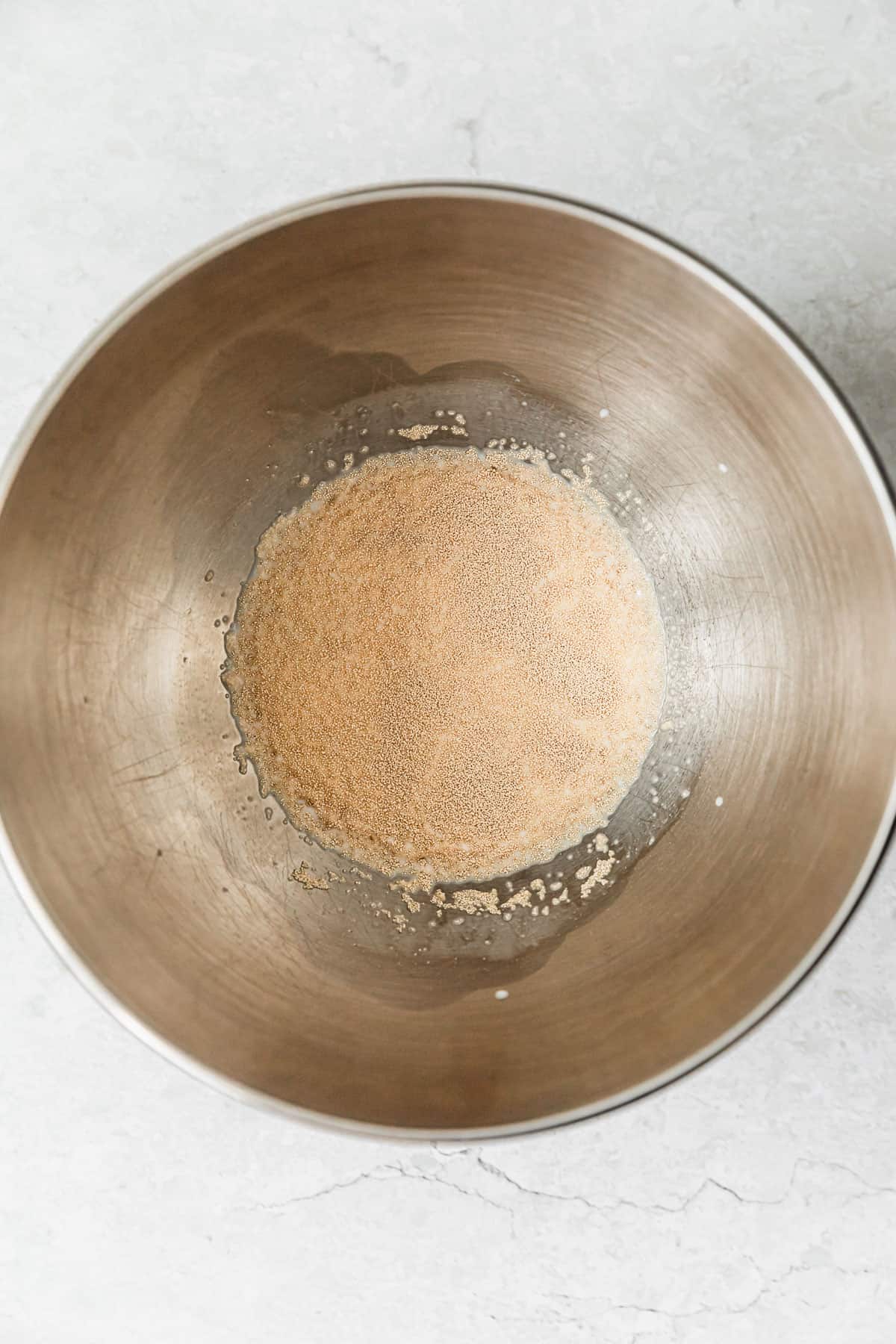 A silver bowl with milk and yeast on a white counter.