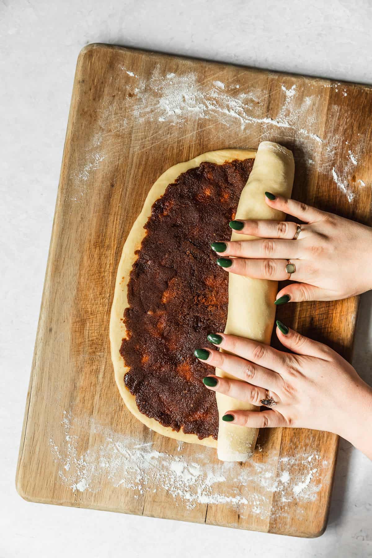 Hands rolling small batch cinnamon rolls on a wood board.