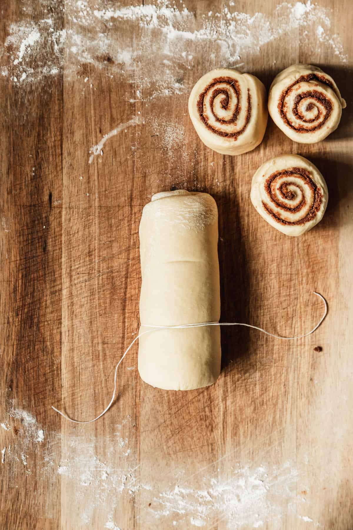 A cinnamon roll log with floss wrapped around it on a wood board.