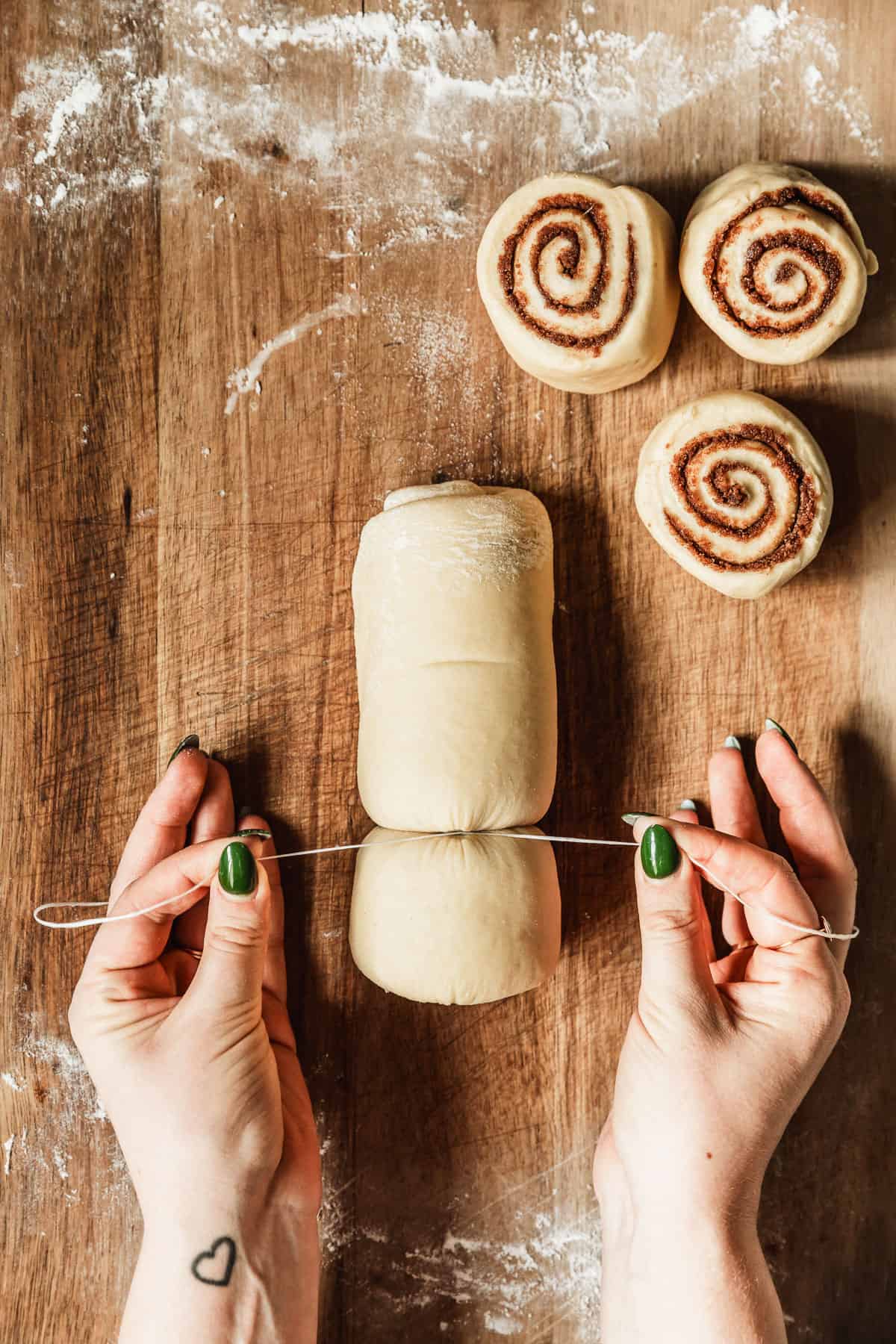 Hands using floss to slice small batch cinnamon rolls on a wood table.