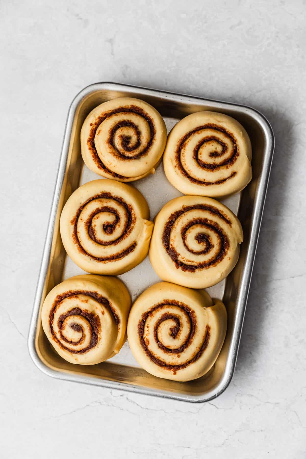 Puffy small batch cinnamon rolls in a pan on a marble counter.