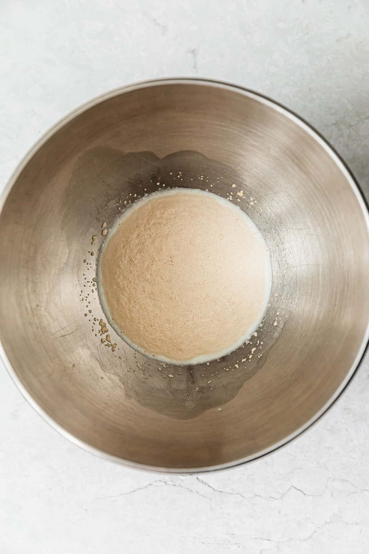 A silver bowl of puffy yeast on a white counter.