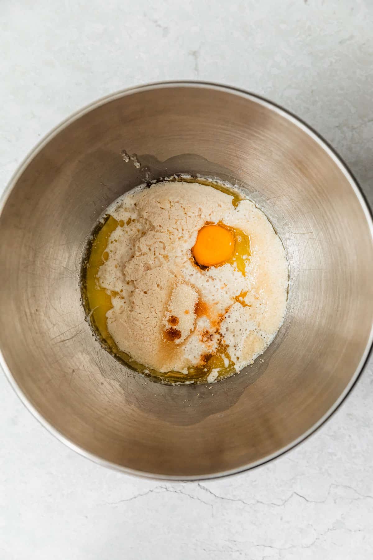 A silver bowl of yeast, sugar, an egg, and vanilla on a white backdrop.