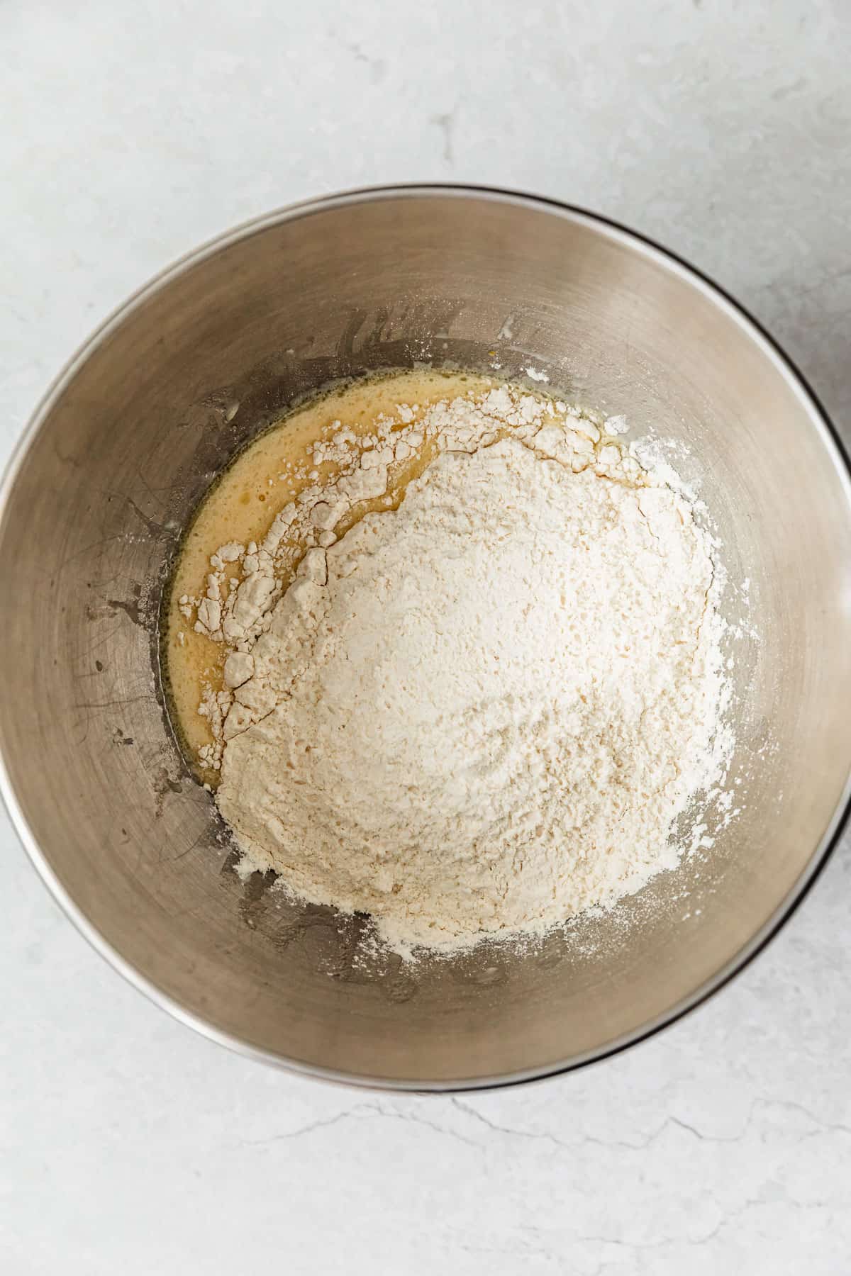 A silver bowl with butter, sugar, yeast, and flour on a white counter.