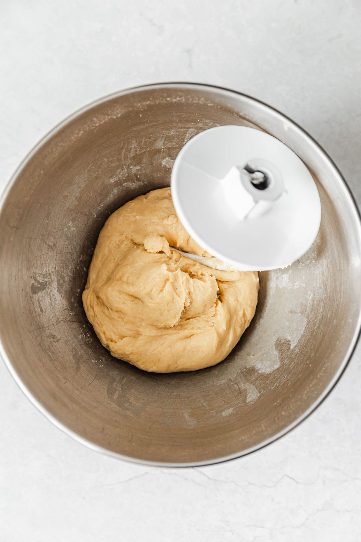 A silver bowl of dough with a dough hook on a white counter.