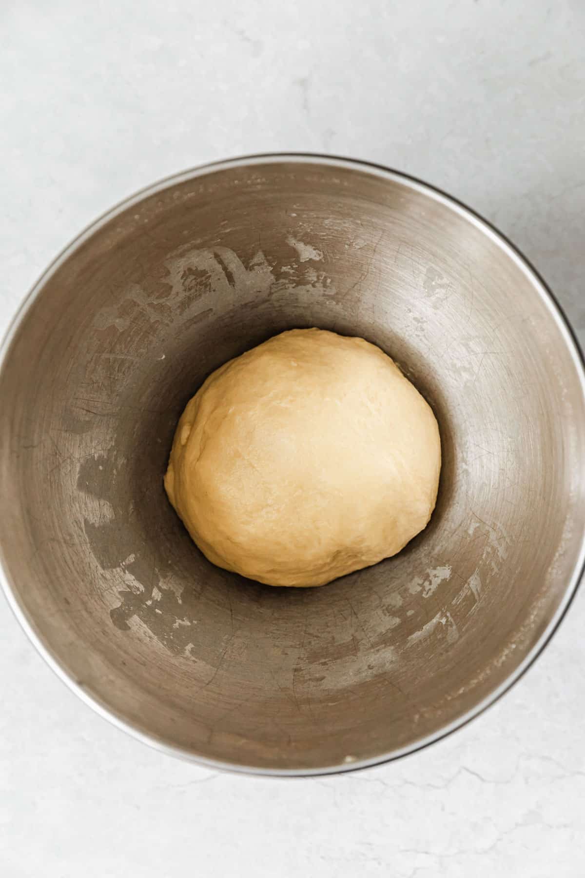 A silver bowl with small batch cinnamon rolls dough on a marble table.