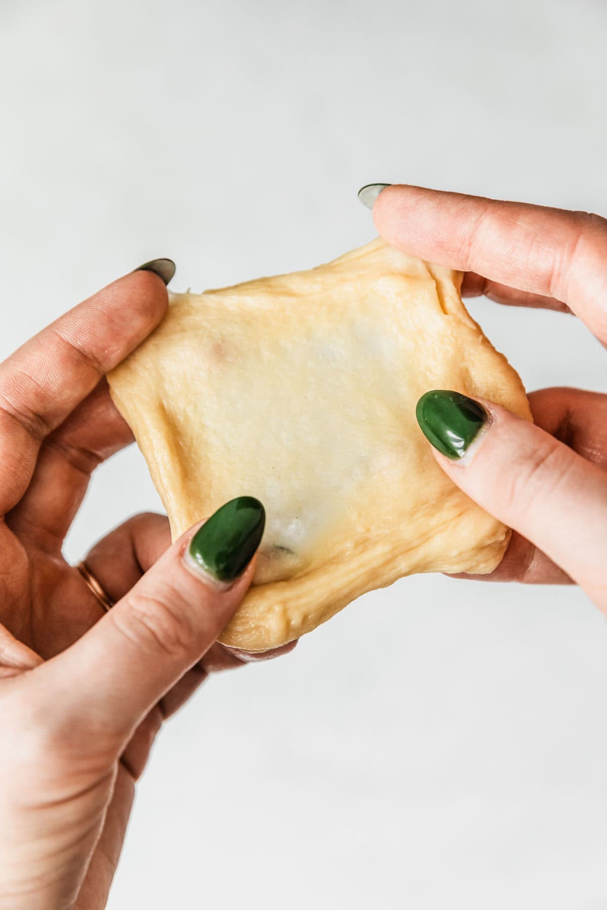 Hands spreading dough to do the windowpane test.