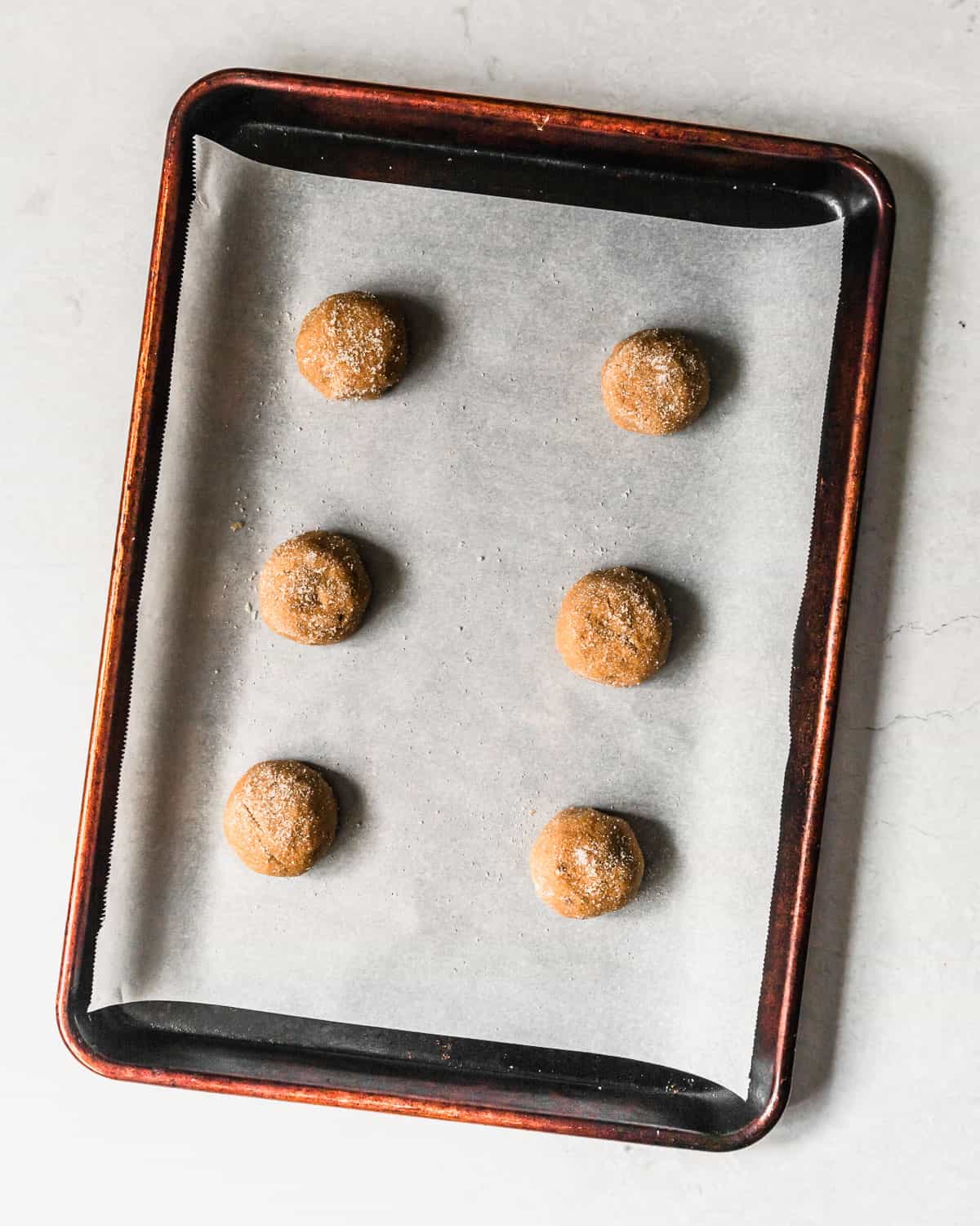 A sheet pan with raw small batch peanut butter cookies on a marble table.