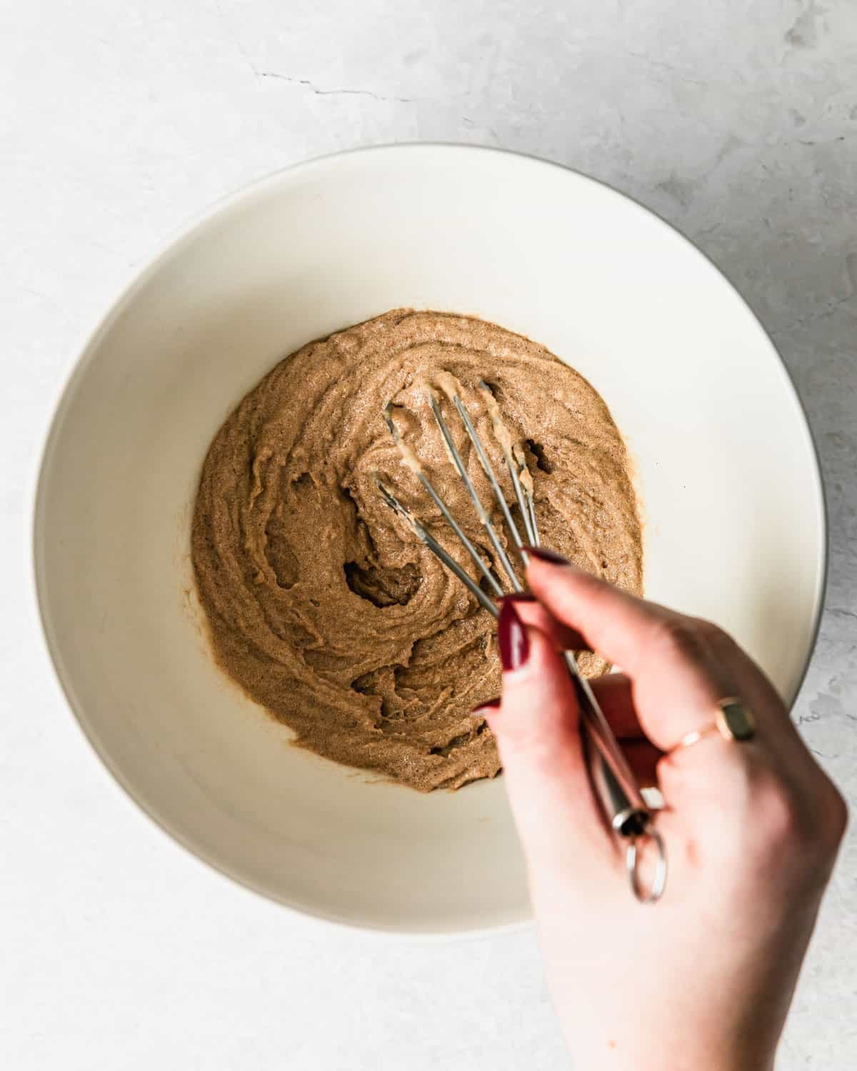 A hand whisking butter and brown sugar in a white bowl.