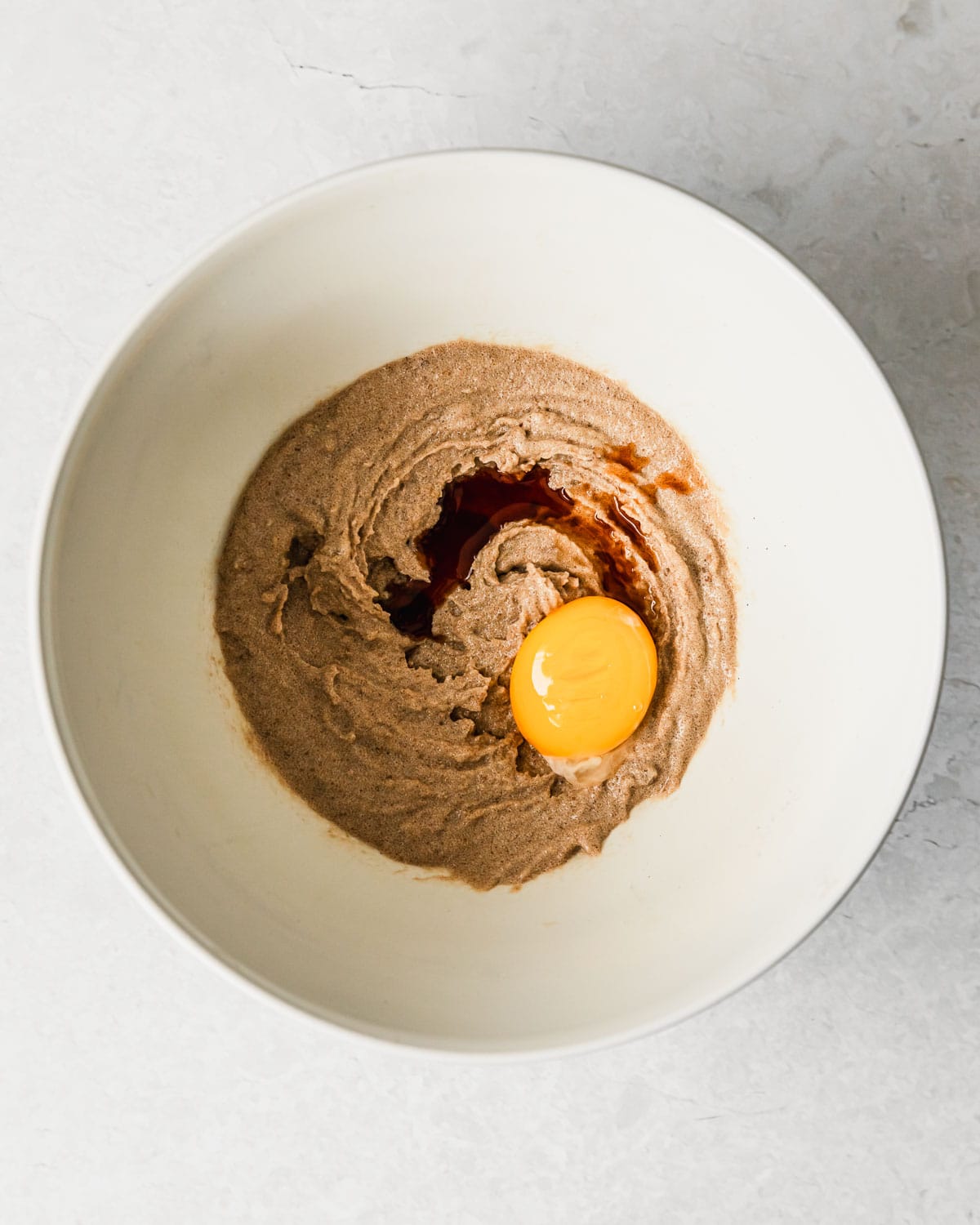 A white bowl of butter, sugar, vanilla, and an egg yolk on a grey counter.