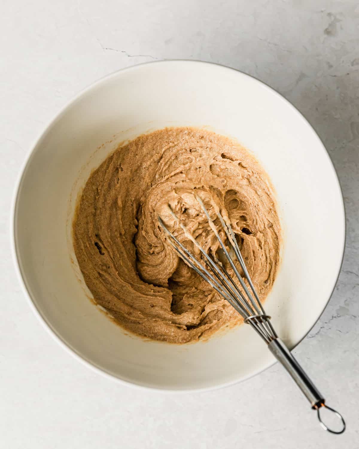 A white bowl of creamed butter, brown sugar, and an egg yolk on a white counter.