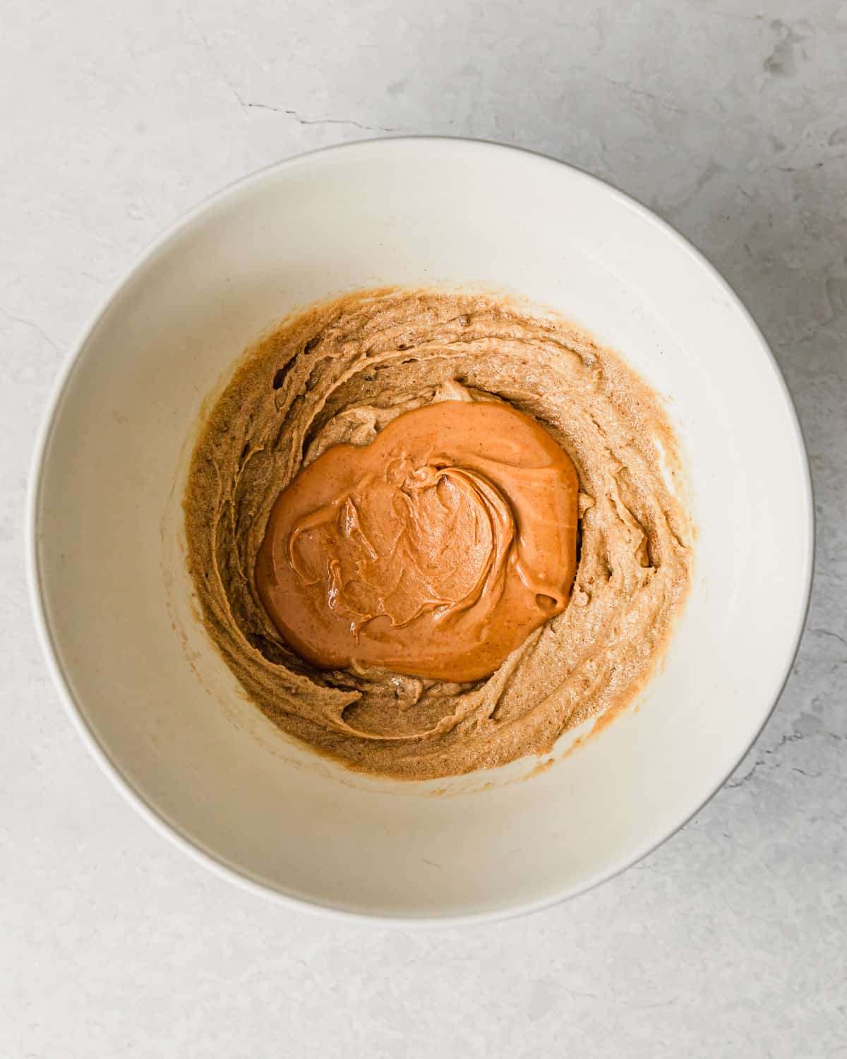 A white bowl with creamed butter, sugar, and peanut butter on a marble counter.