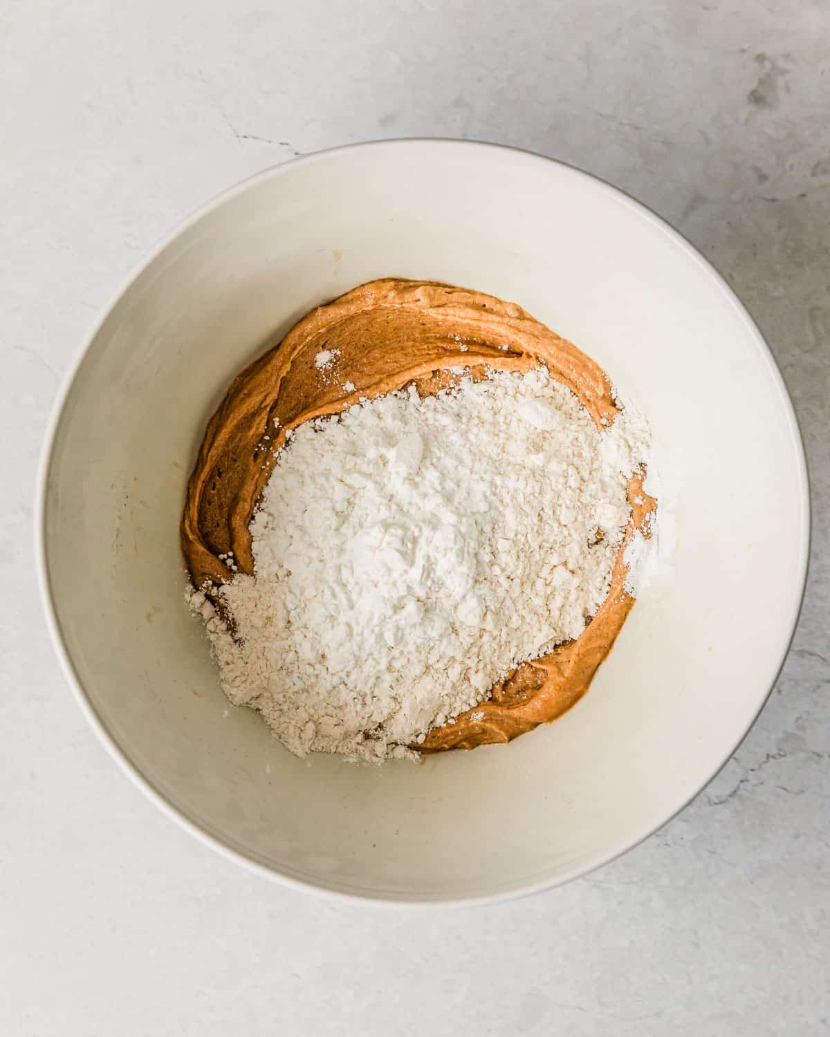 A white bowl with peanut butter mixture and flour on a white counter.
