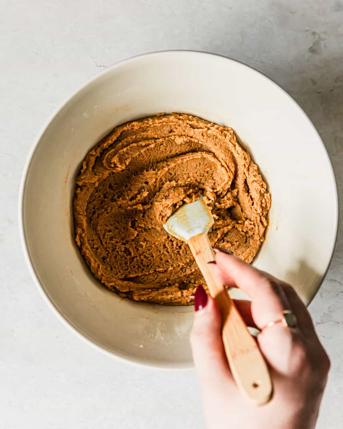 A hand using a rubber spatula to stir small batch peanut butter cookies dough in a white bowl.