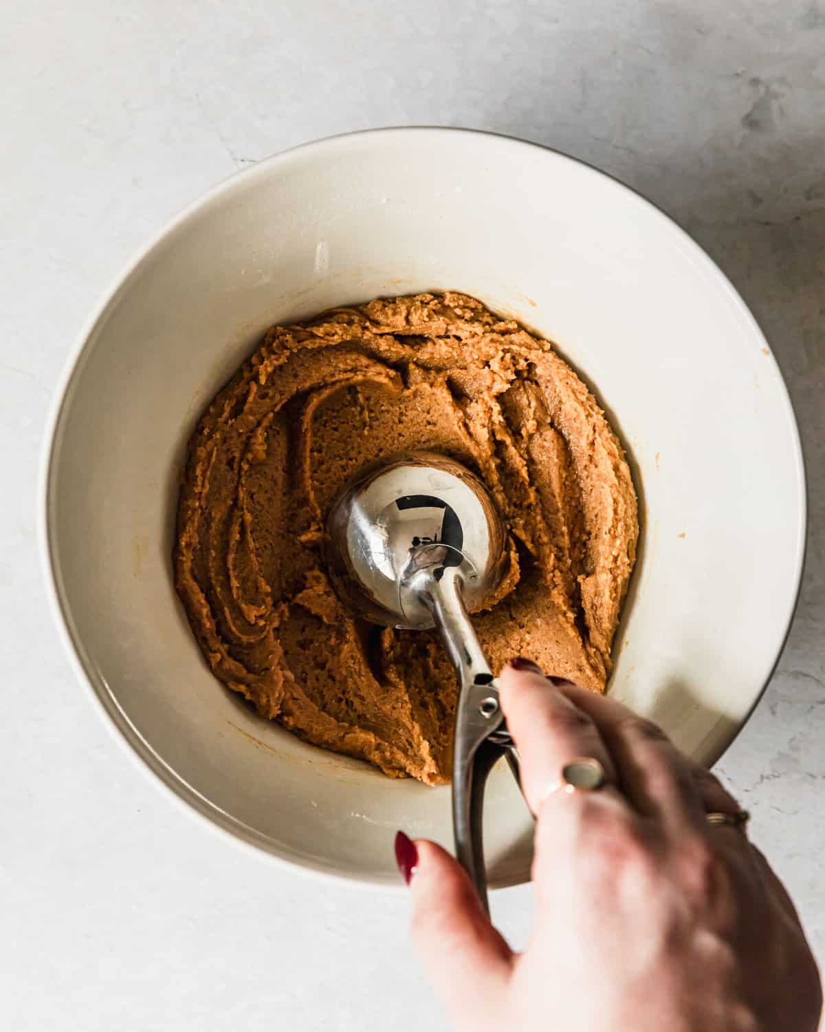 A hand using a scoop to scoop small batch peanut butter cookies out of a white bowl.
