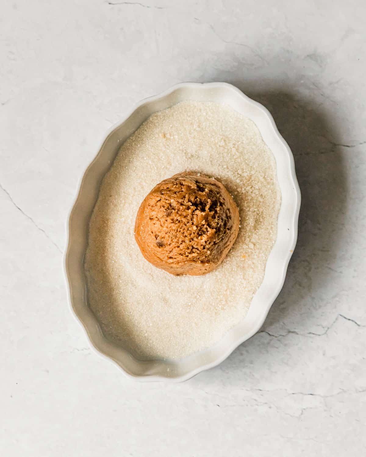 A white dish of sugar with a small batch peanut butter cookie on a white counter.