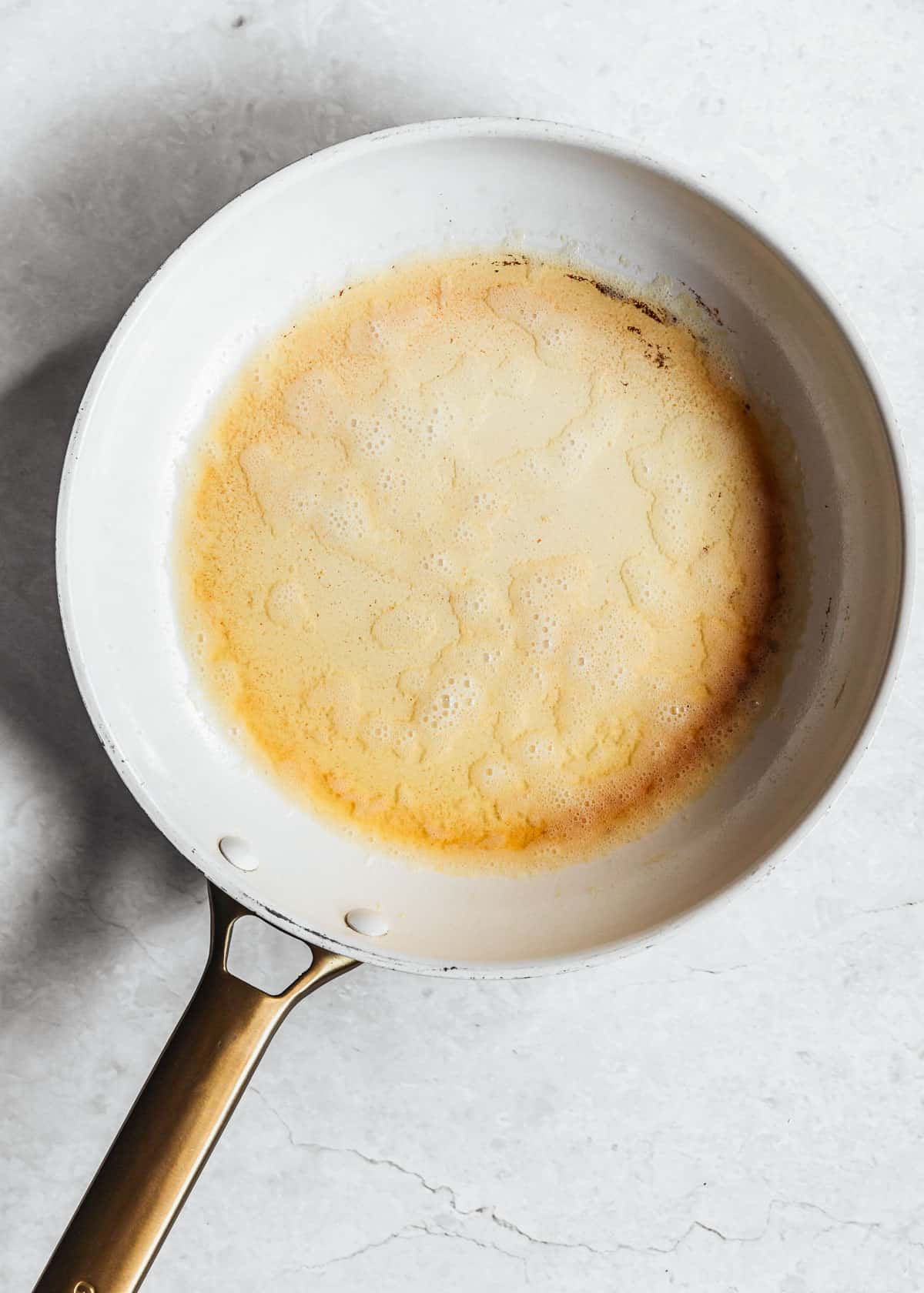 A white pan of brown butter on a white counter.
