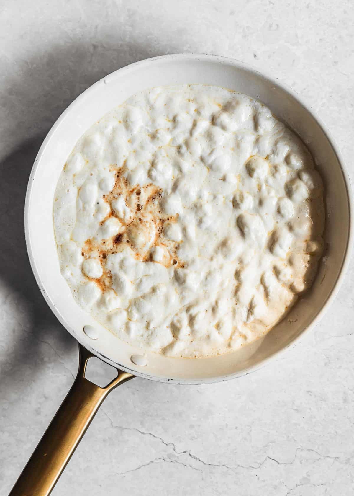 A white pan with butter, marshmallows, and vanilla on a white counter.