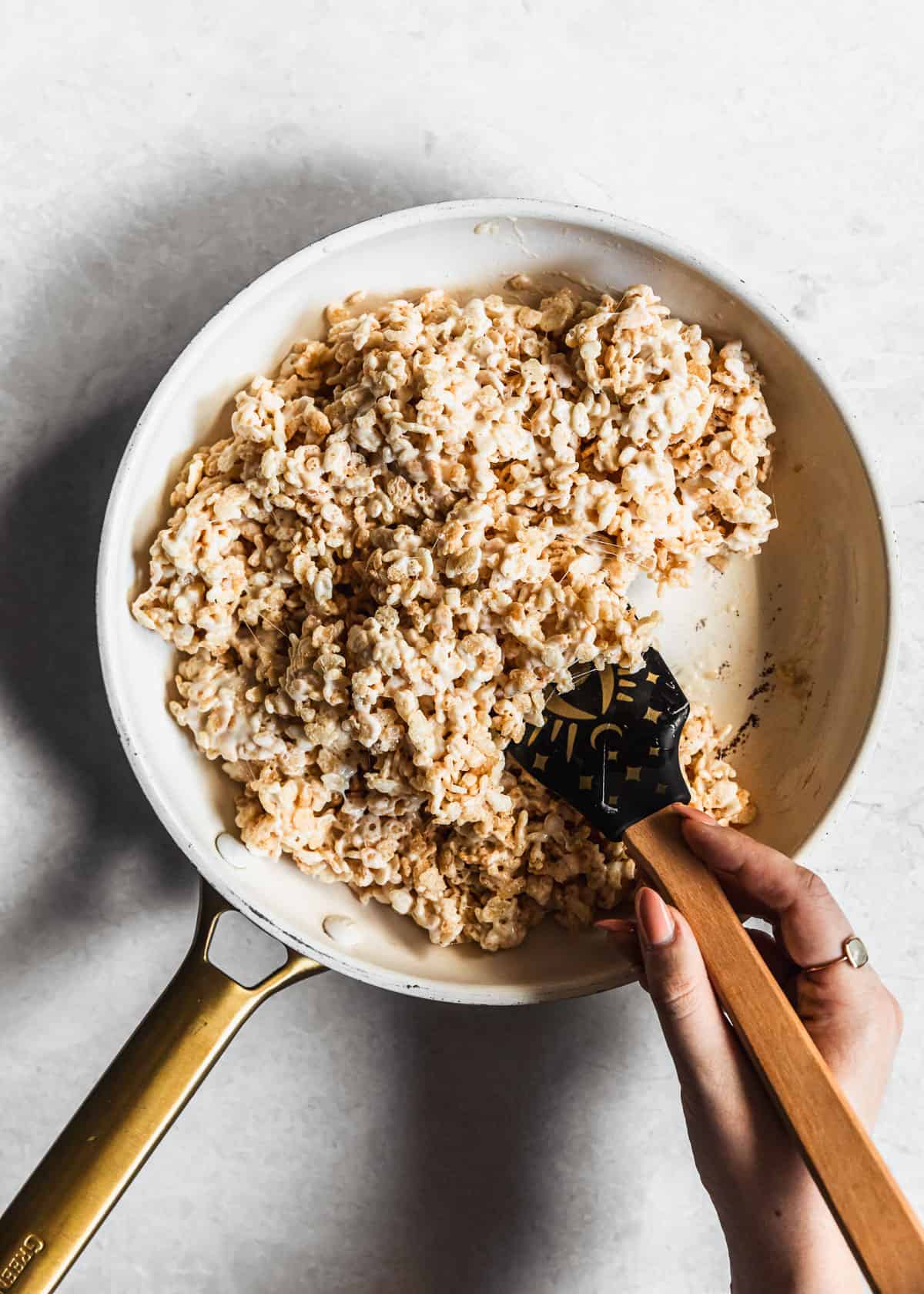 A hand stirring a white pan of small batch rice Krispies treats mixture on a white counter.