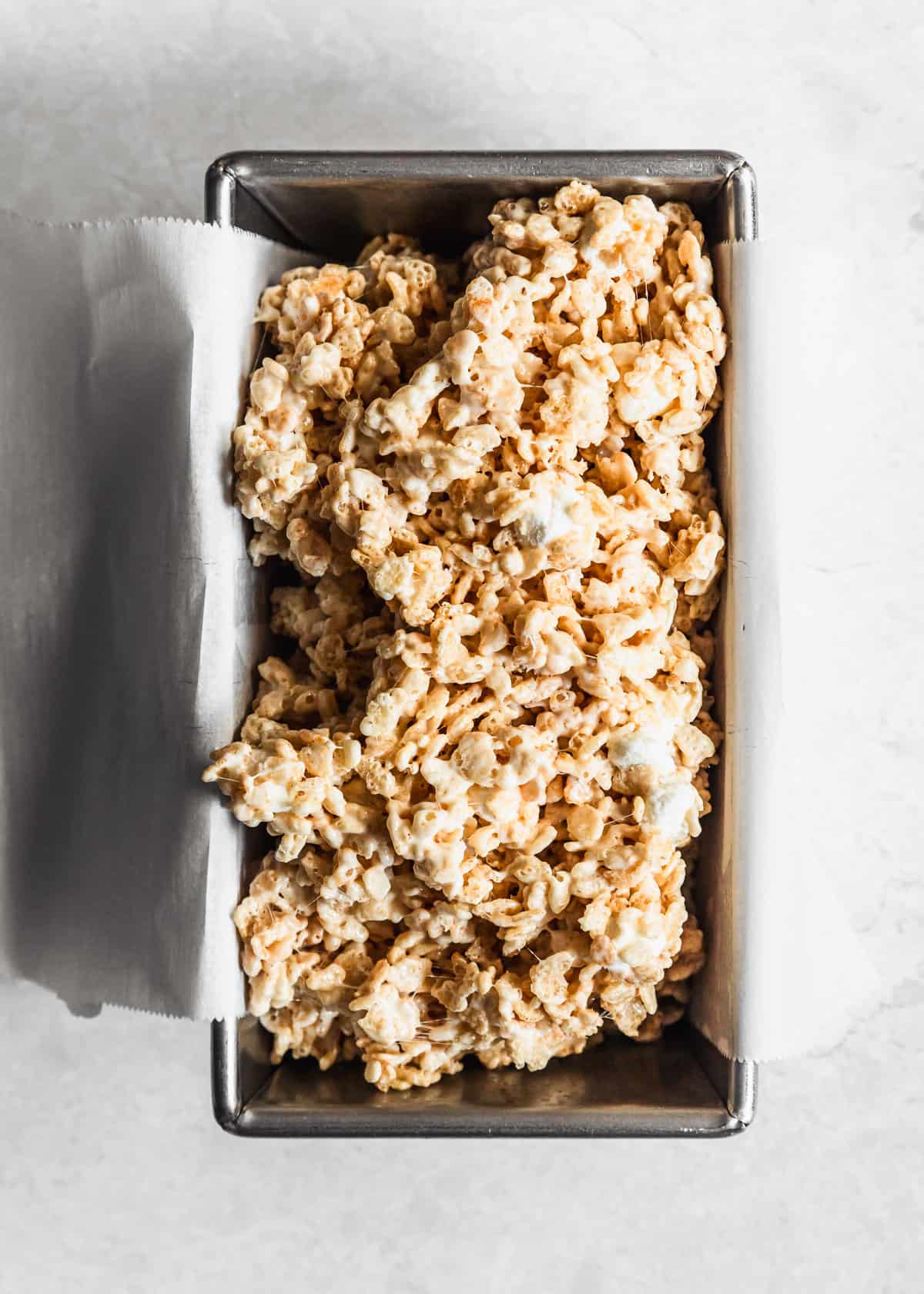 A loaf pan with small batch Rice Krispies treats mixture on a white table.