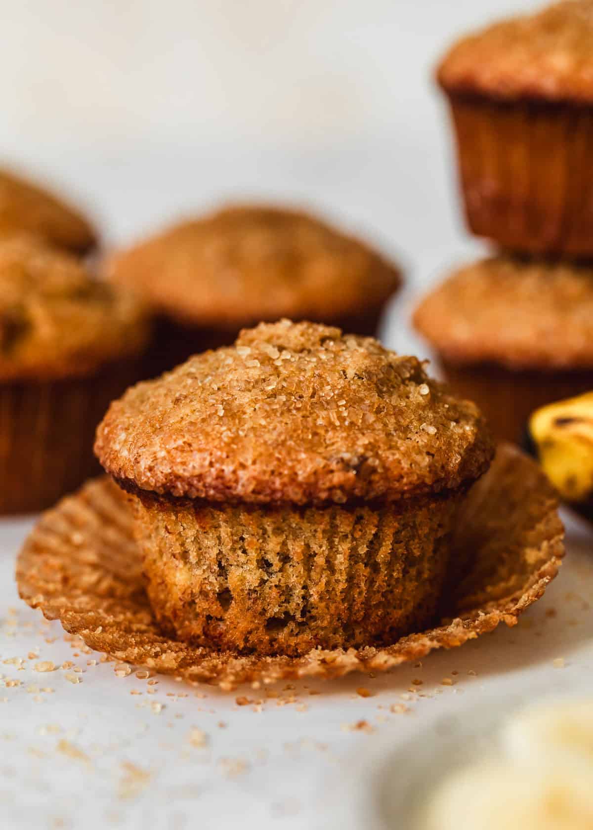 A batch of small batch banana muffins on a white counter next to a white bowl of bananas.