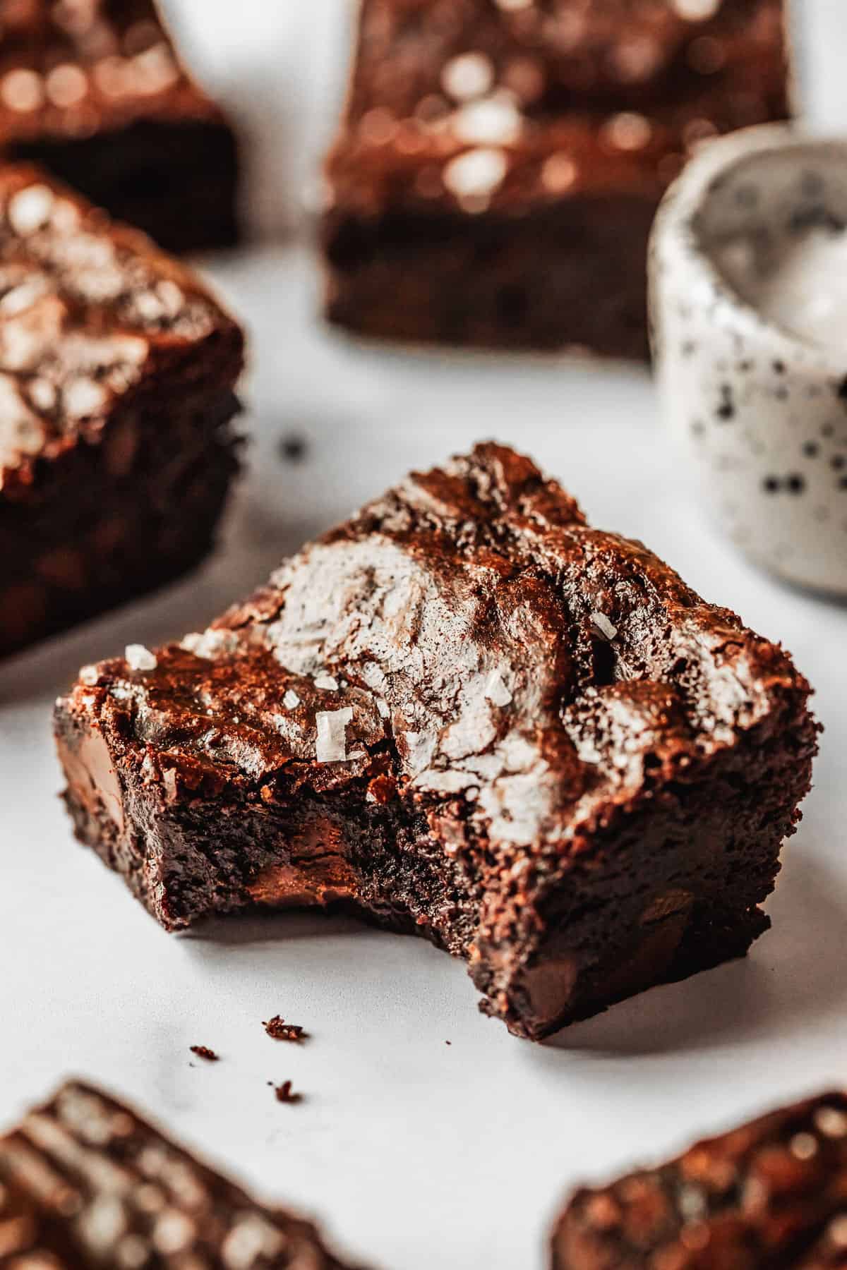 A brownie with a bite taken out of it on a white counter next to rows of small batch brownies and a white bowl of salt.