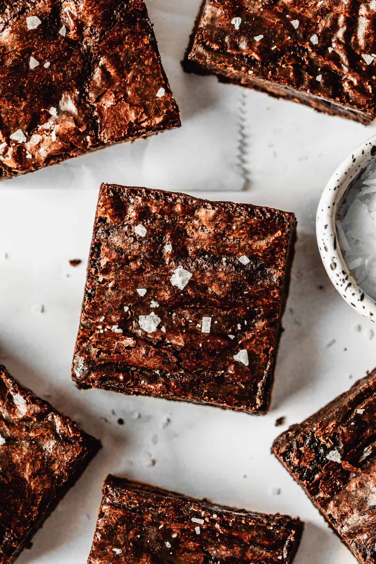 Rows of small batch brownies on a white counter next to a white bowl of salt.
