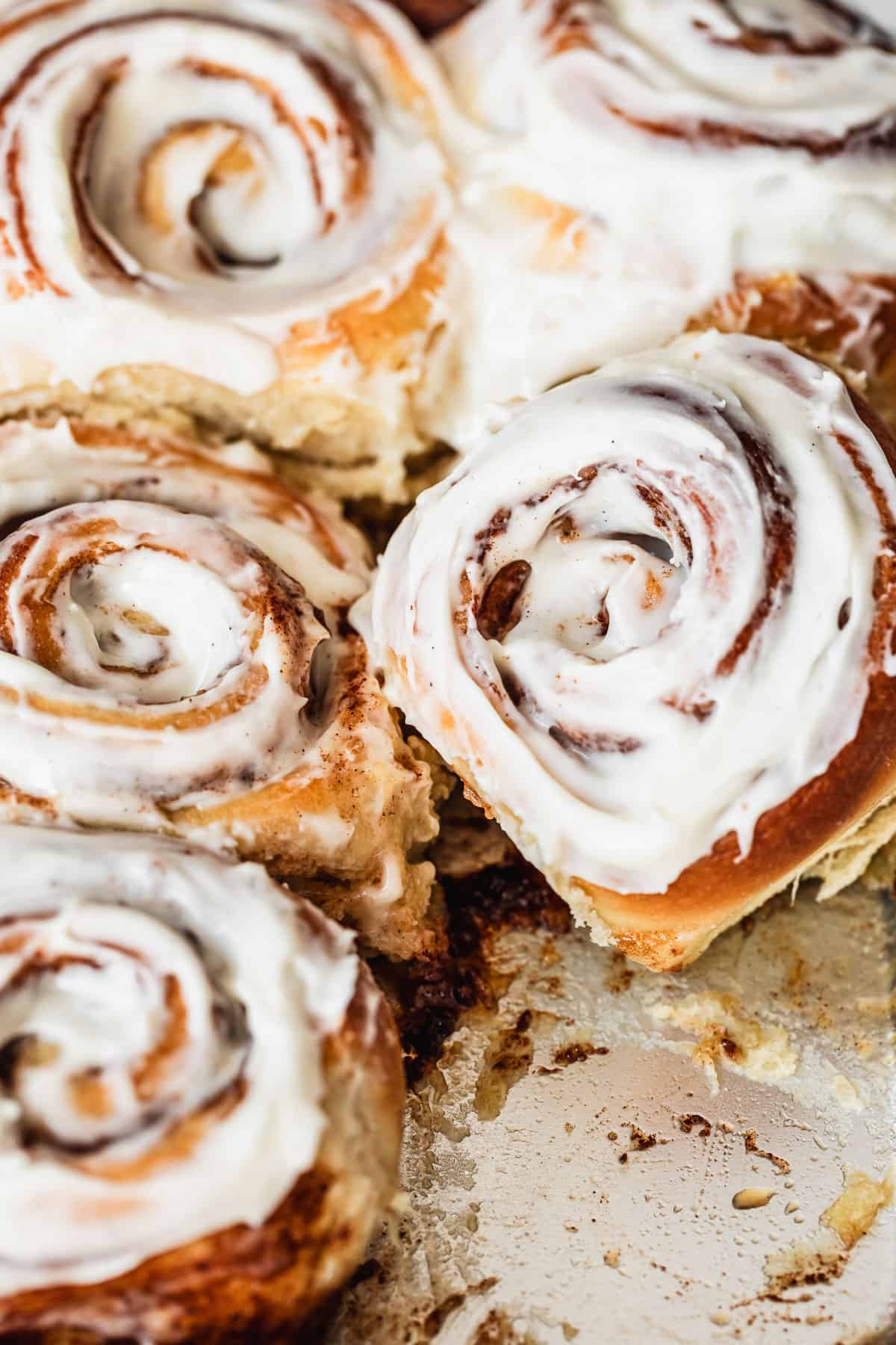 A cinnamon roll leaning against a row of small batch cinnamon rolls on a silver pan.