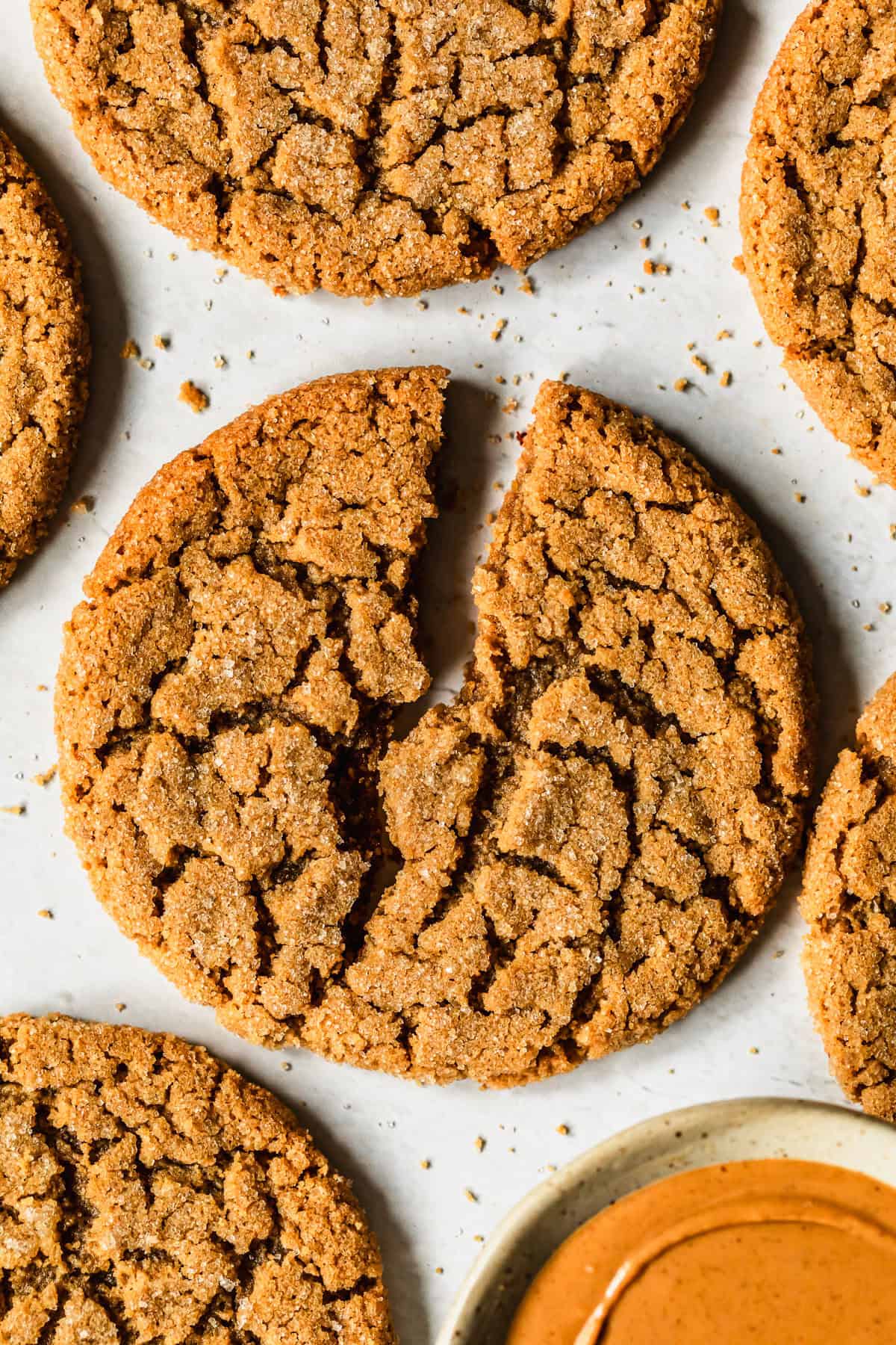 A halved cookie on a white marble counter next to rows of small batch peanut butter cookies.