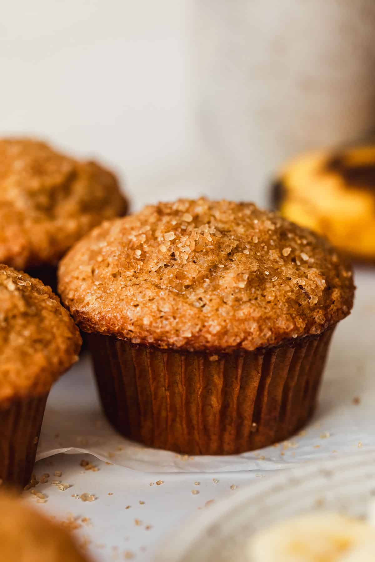 Rows of small batch banana muffins on a white counter next to a banana and a white bowl of banana slices.