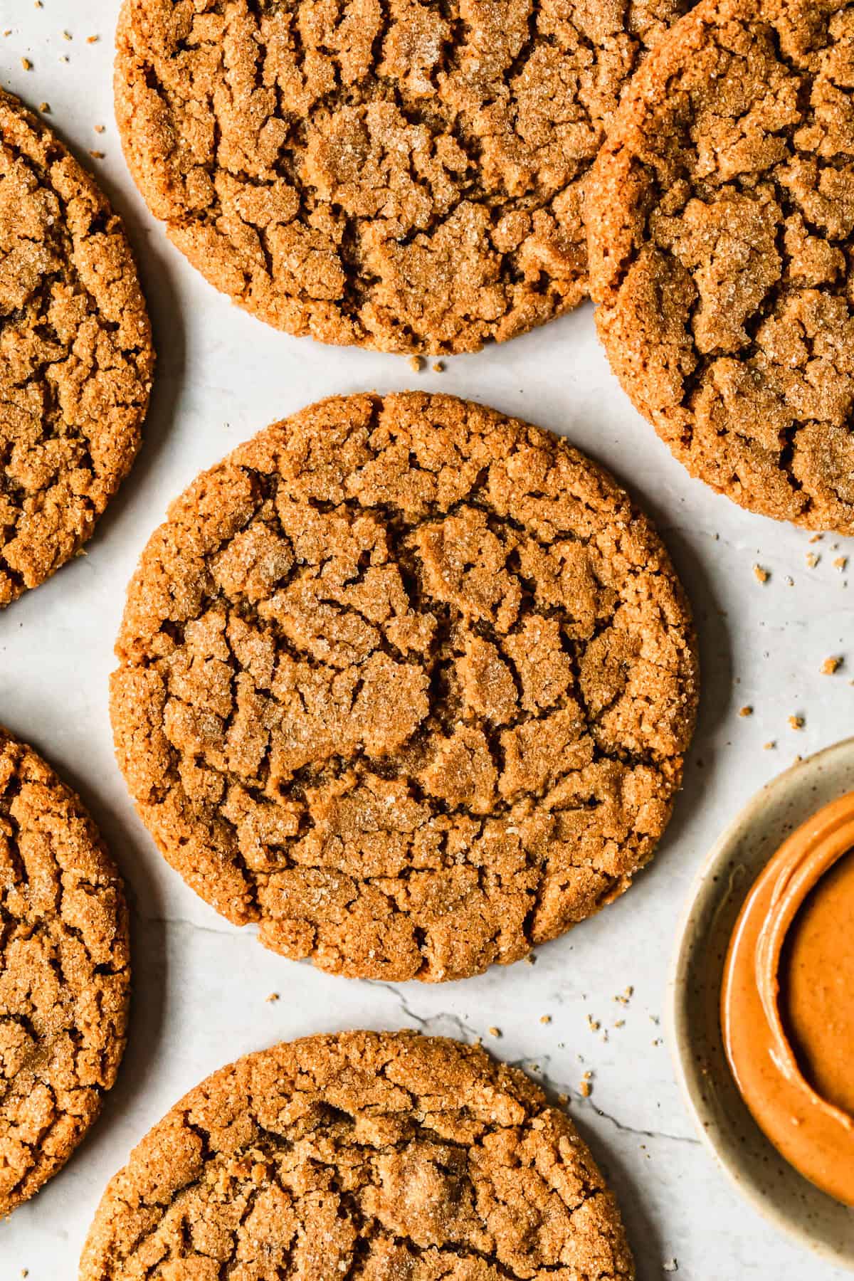 Rows of small batch peanut butter cookies and a white bowl of peanut butter on a marble counter.