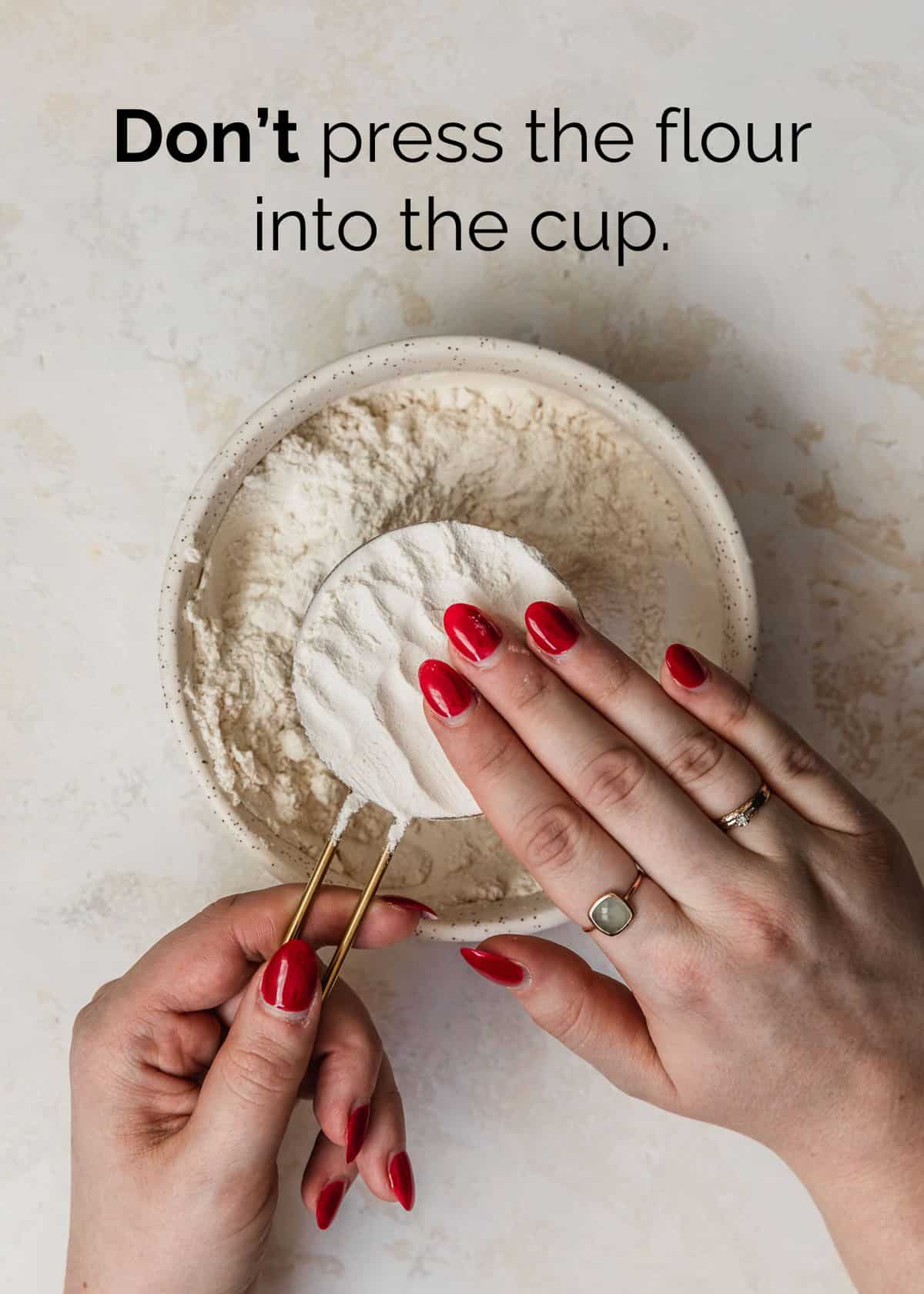 Measuring ingredients for small batch baking. A hand pressing flour into a gold measuring cup.
