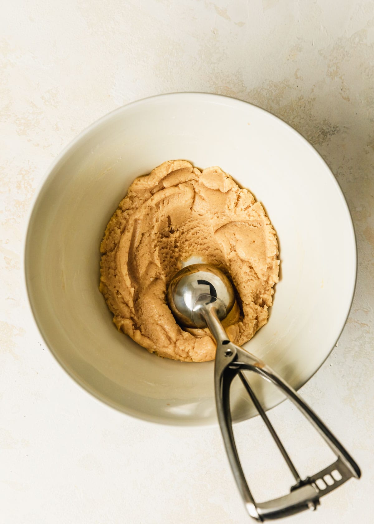a cookie scoop scooping small batch snickerdoodles out of a white bowl on a beige table.