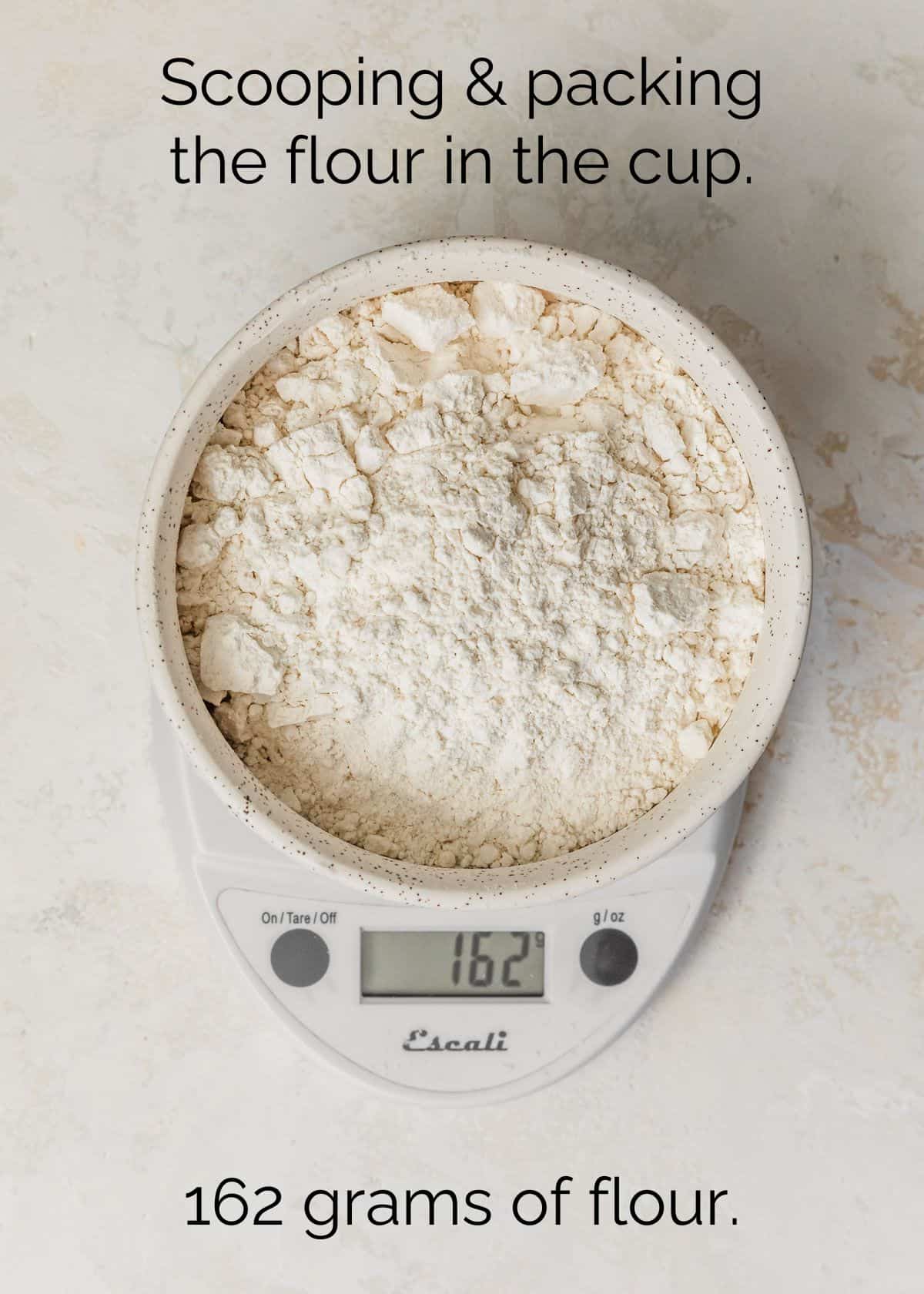 A white bowl of flour on a scale with a tan stone backdrop.