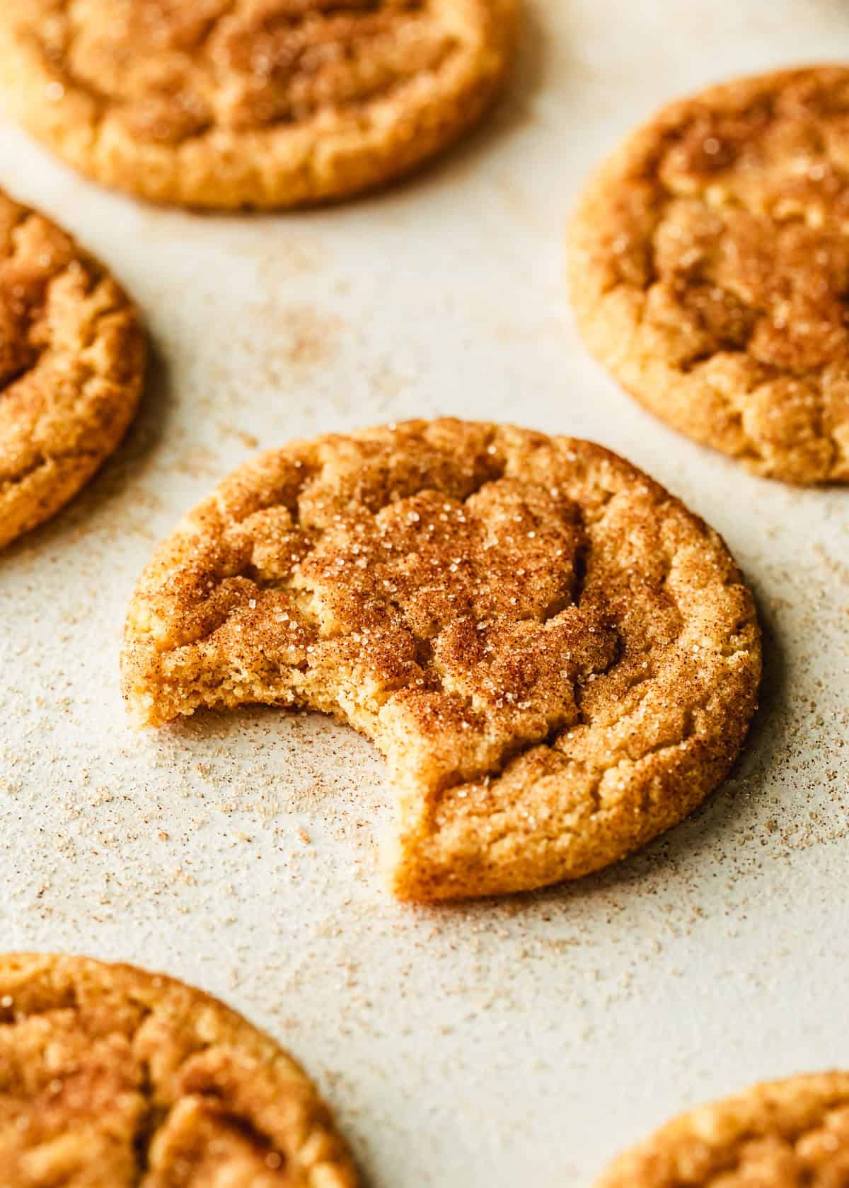 A cookie with a bite taken out of it on a tan counter next to rows of small batch snickerdoodles.